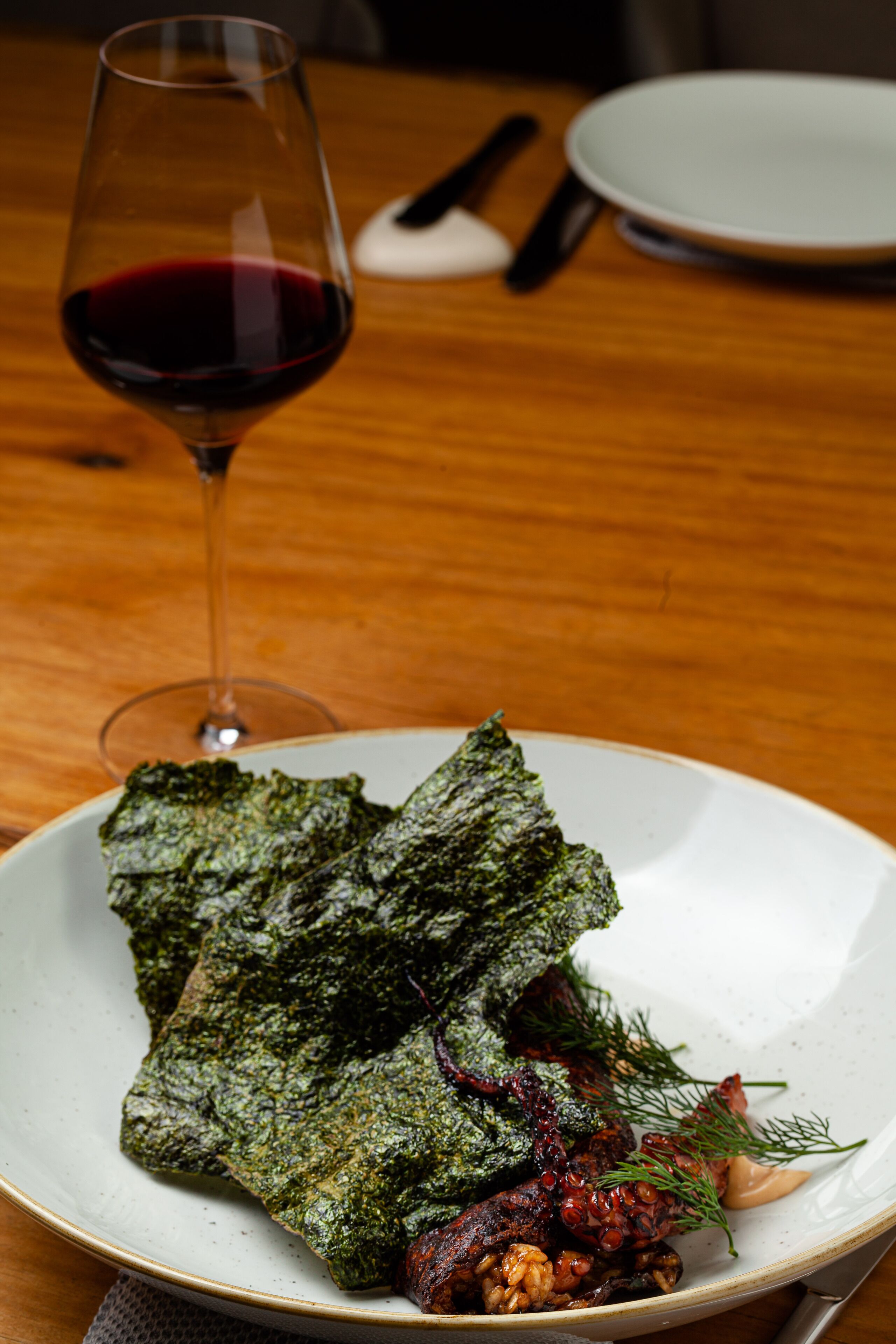Ein Teller mit Speisen, Grünzeug und ein Glas Rotwein auf einer Holztischplatte.