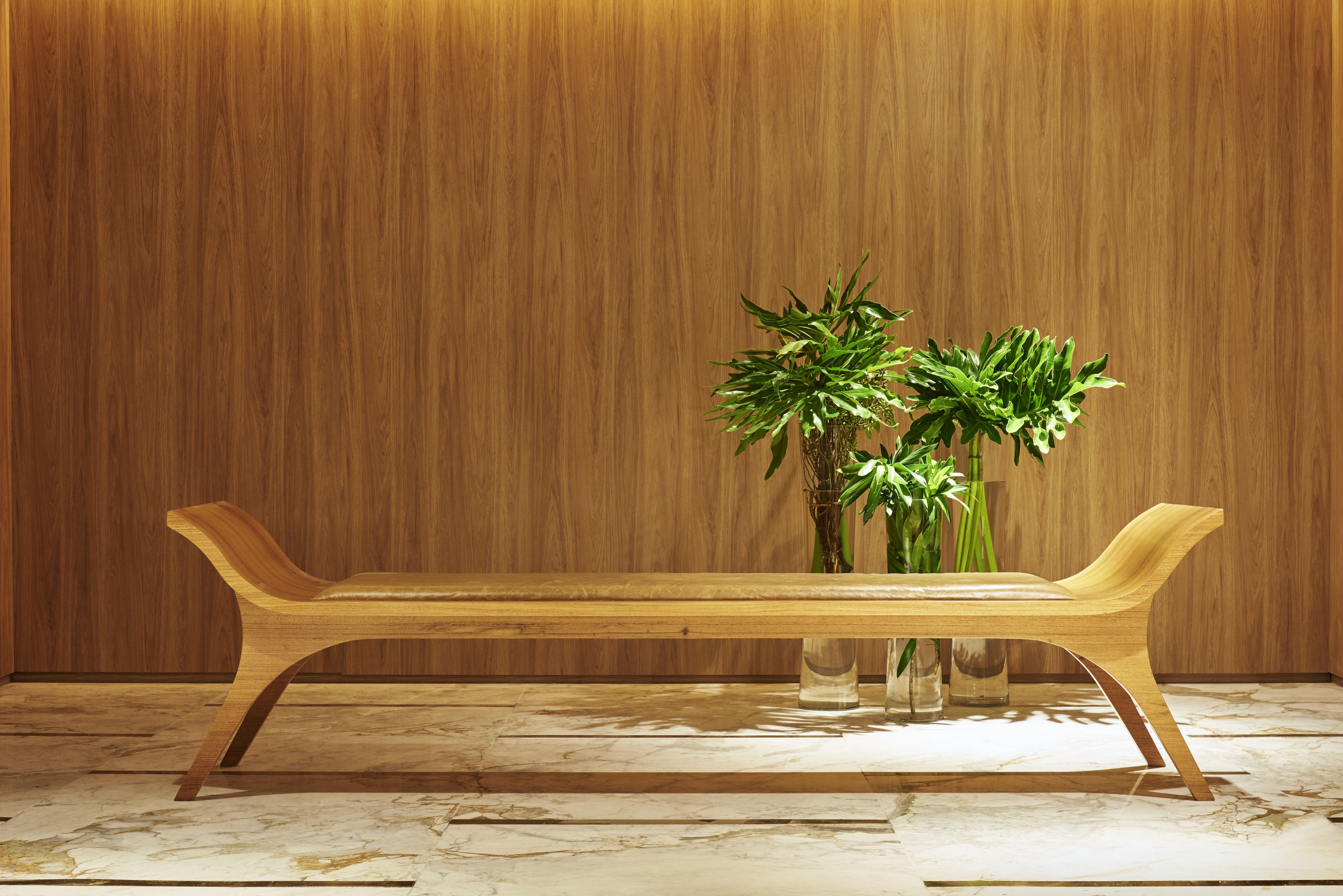A wooden bench with a vase of green plants against a wooden wall.