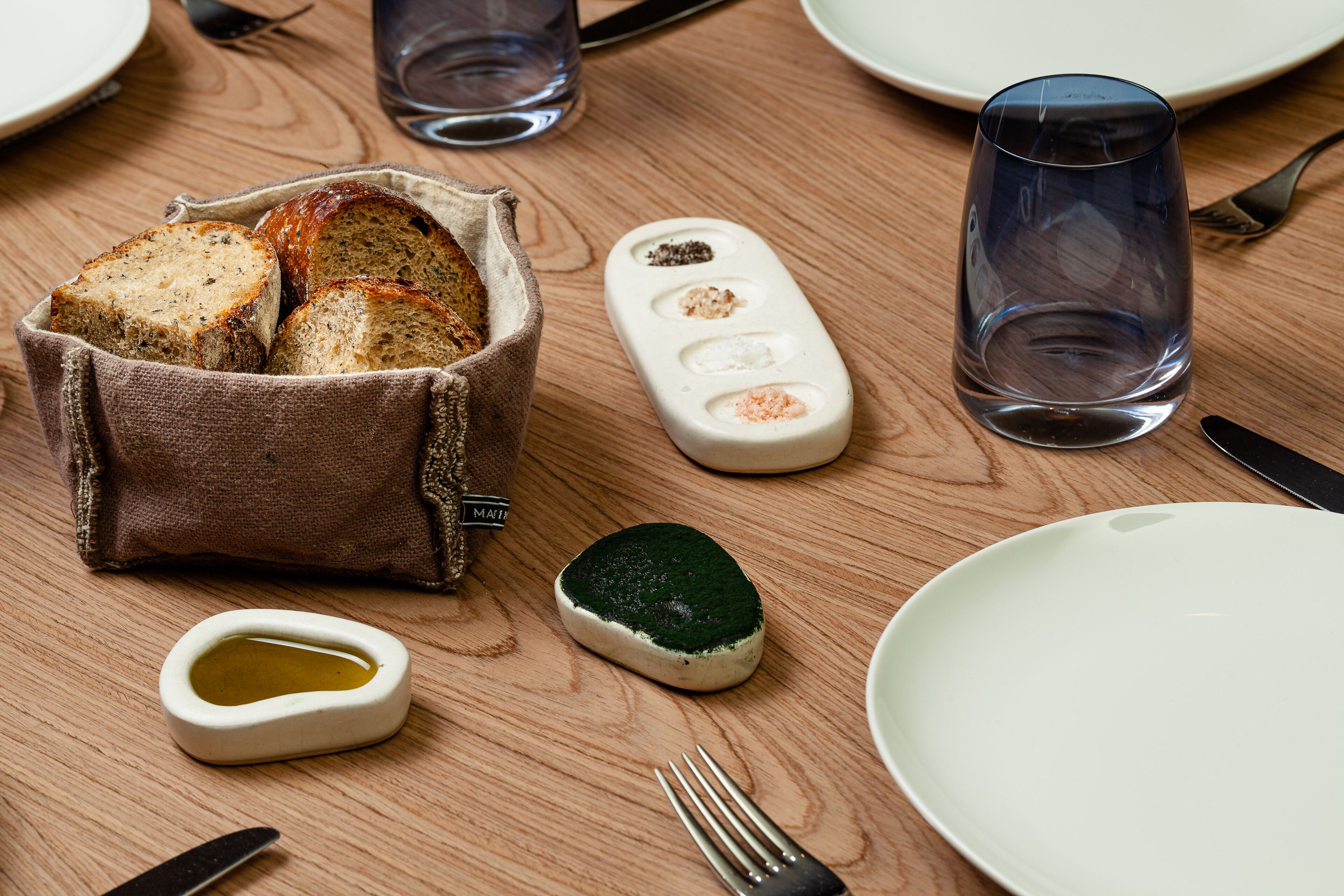 A wooden table with a loaf of bread, a salt shaker, a glass of water, a small dish of oil, and a fork.