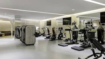 Academia moderna com diversos equipamentos de exercício, um espelho grande e uma área de descanso com sofá.
