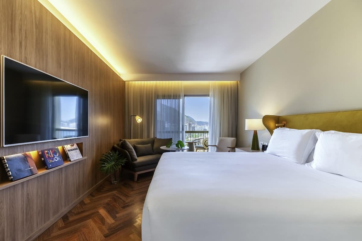 Ein Hotelzimmer mit einem großen Bett, einem Flachbildfernseher, einer Sitzecke, einem Schreibtisch und Blick auf die Stadt.