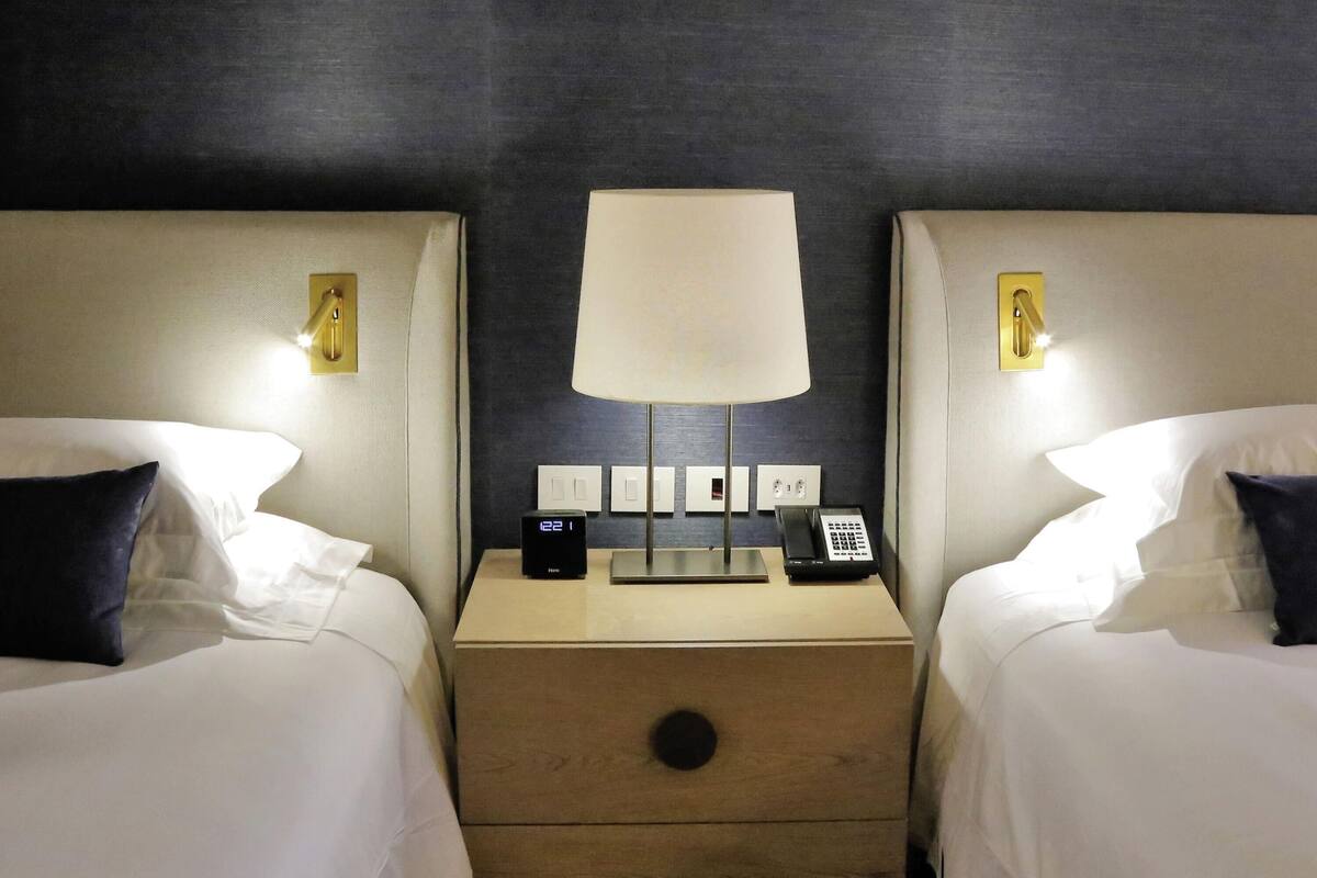 Ein Hotelzimmer mit zwei Betten, einem Nachttisch mit Lampe, einer digitalen Uhr und einem Telefon.