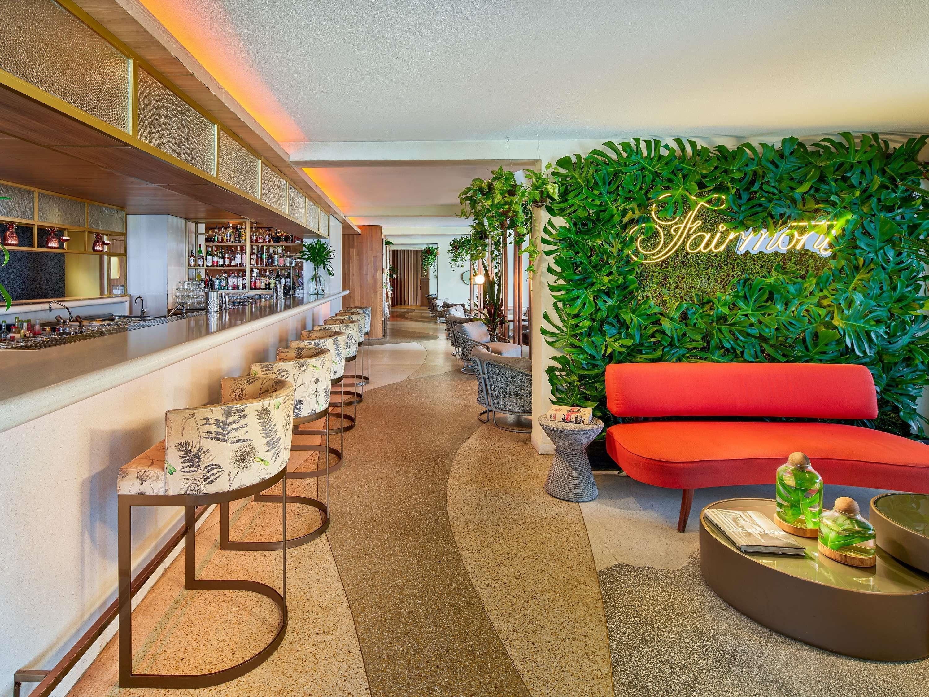 A bar area with a long counter, multiple bar stools, and a neon sign.