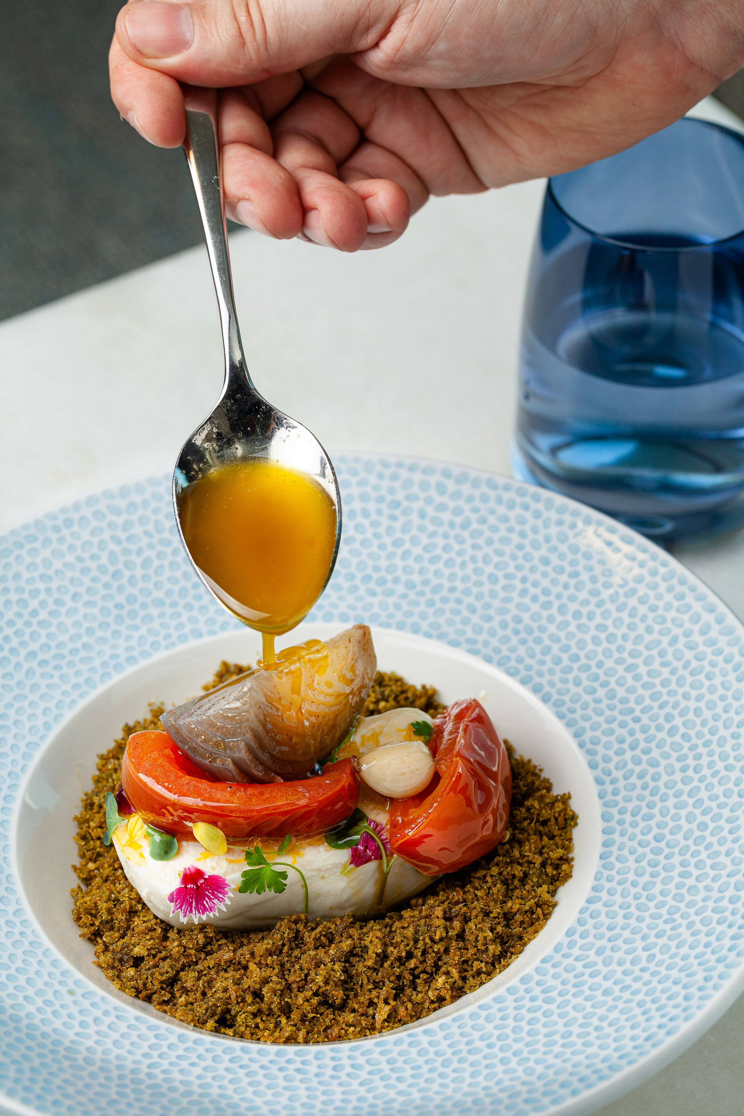 A spoonful of sauce being poured onto a dish with various ingredients.
