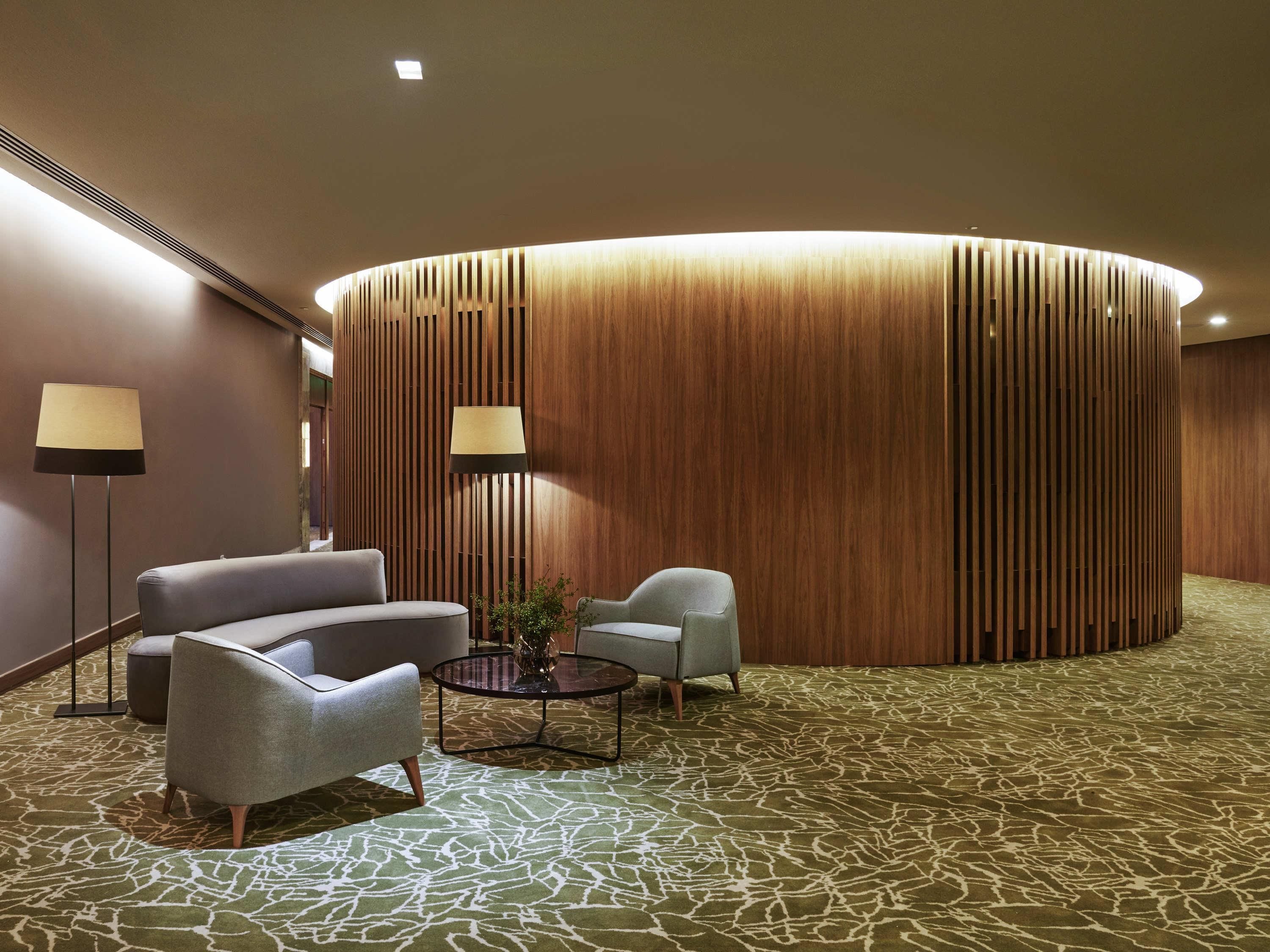 Un hall d’entrée avec un mur en bois incurvé, deux fauteuils, une table basse ronde et des lampes sur pied.