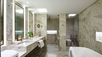 A modern bathroom with marble walls, a large mirror, a bathtub, and a shower area.