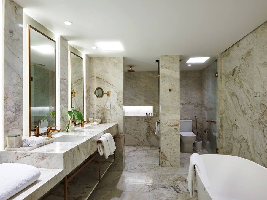 A modern bathroom with marble walls, a large mirror, a bathtub, and a shower area.