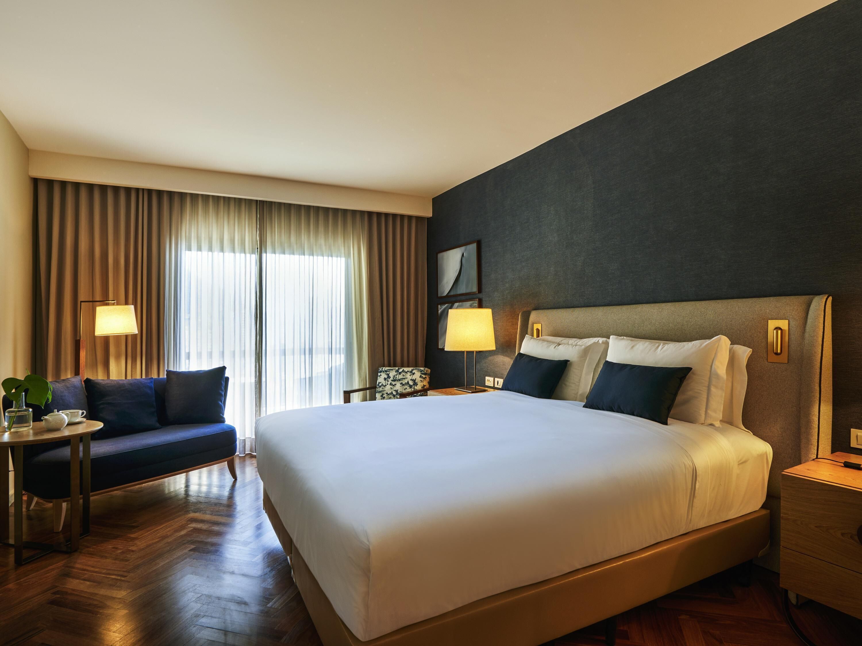 A hotel room with a large bed, a sofa, a desk, and a chair.