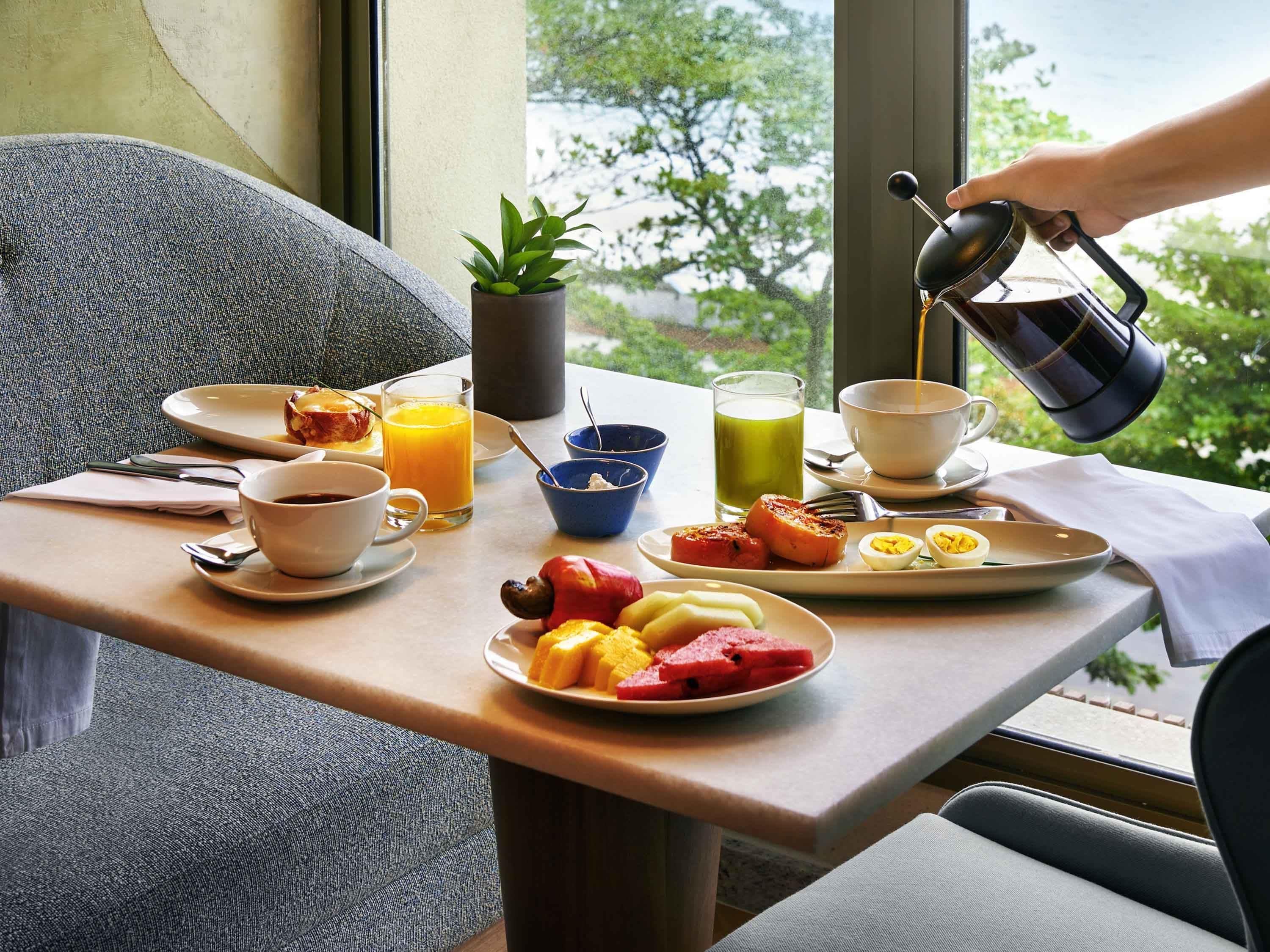 A breakfast table with plates of food, a coffee cup, a glass of orange juice, and a bowl of yogurt.