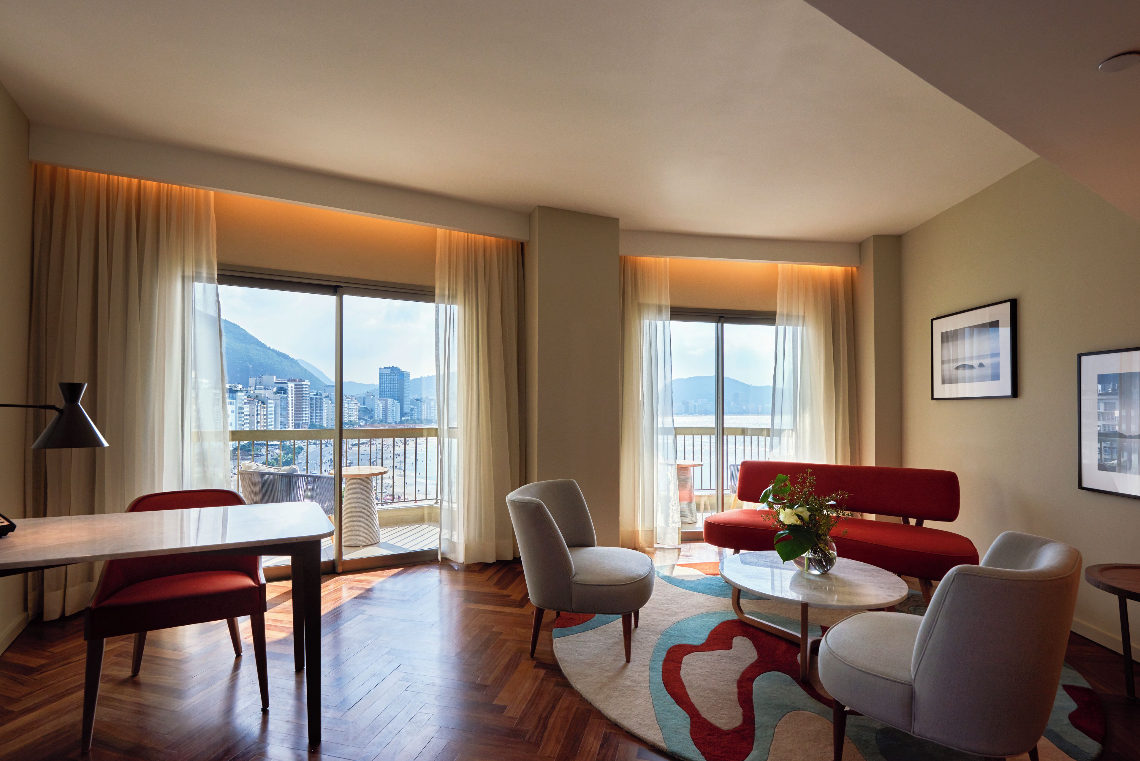 Quarto de hotel moderno com varanda, área de refeições e espaço de estar com vista para a paisagem urbana.