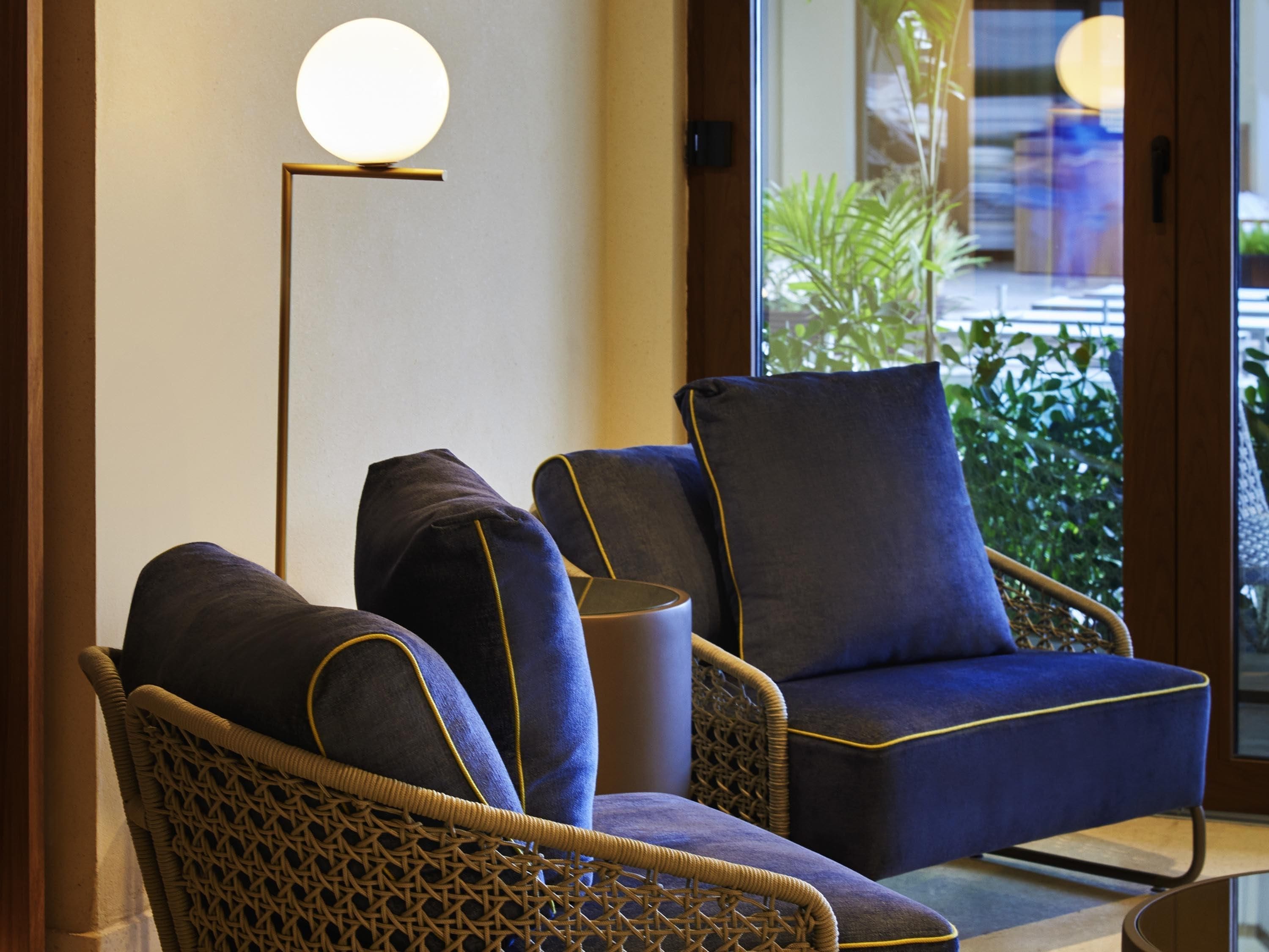 Ein Zimmer mit zwei Sesseln, einer aus Rattan und einer Polstersessel, sowie einer Stehlampe.