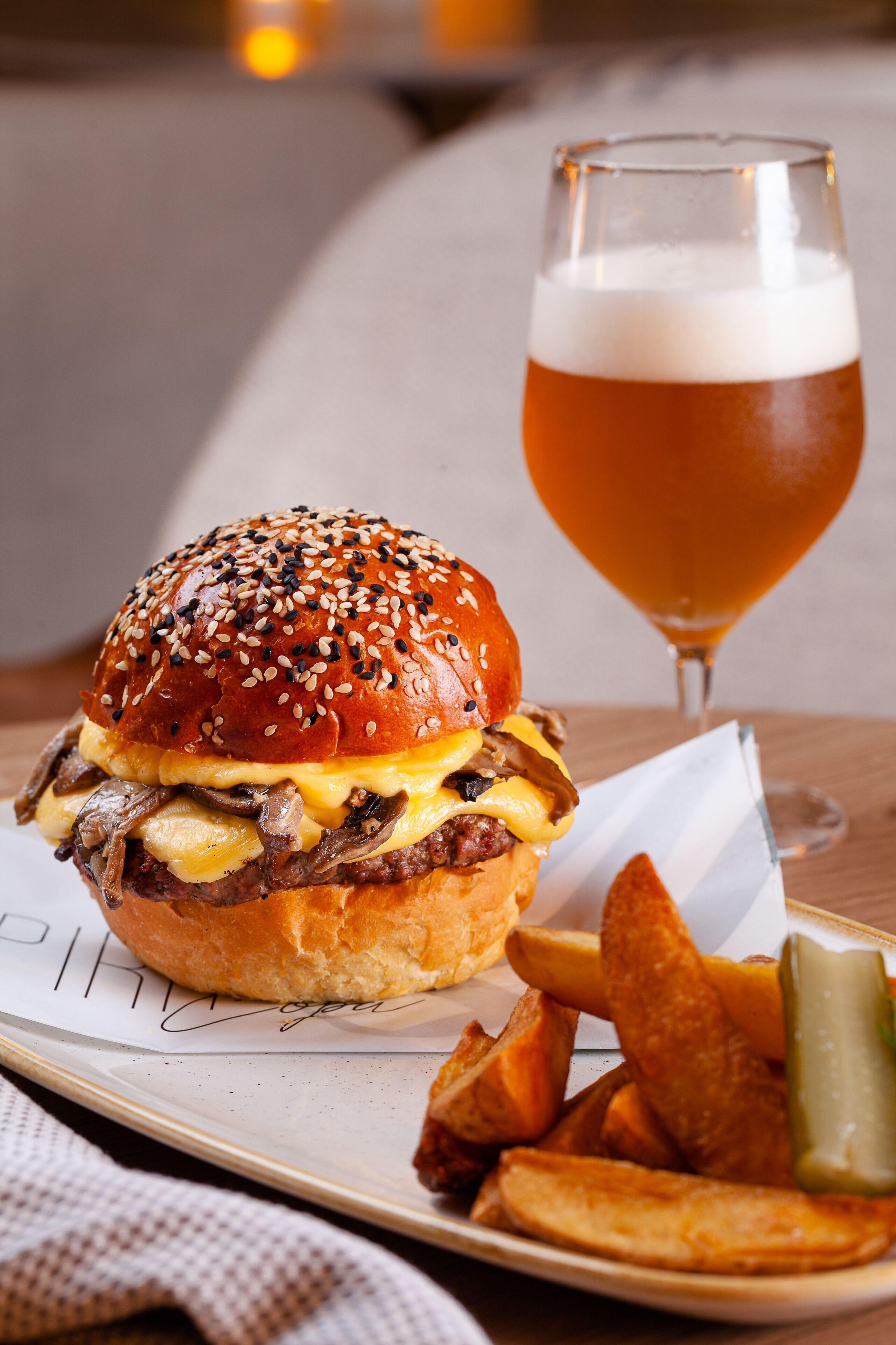A meal consisting of a burger, fries, and a glass of beer on a plate.