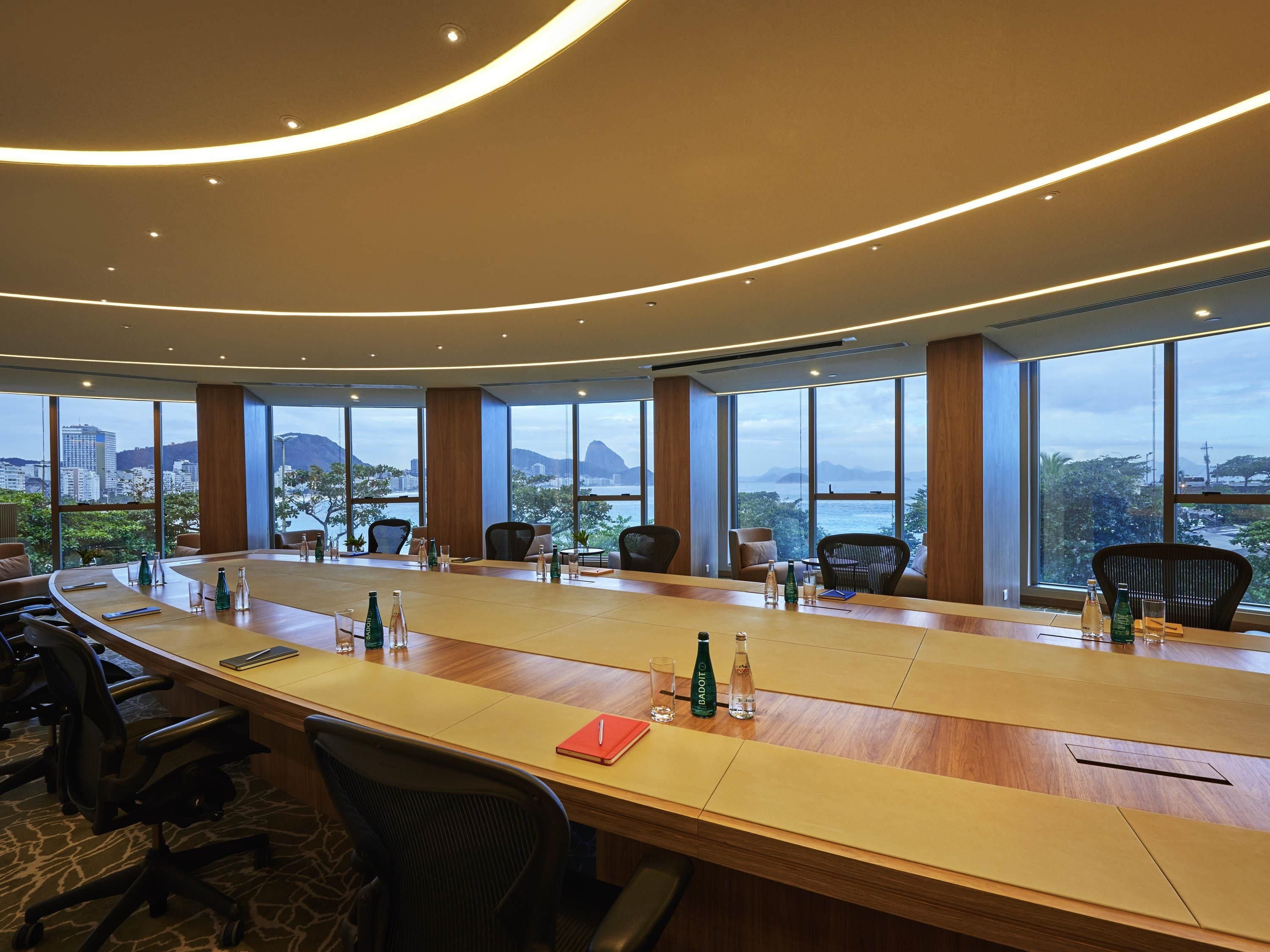 A conference room with a long table, chairs, and large windows offering a city view.