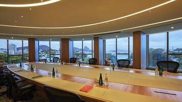 A conference room with a long table, chairs, and large windows offering a city view.