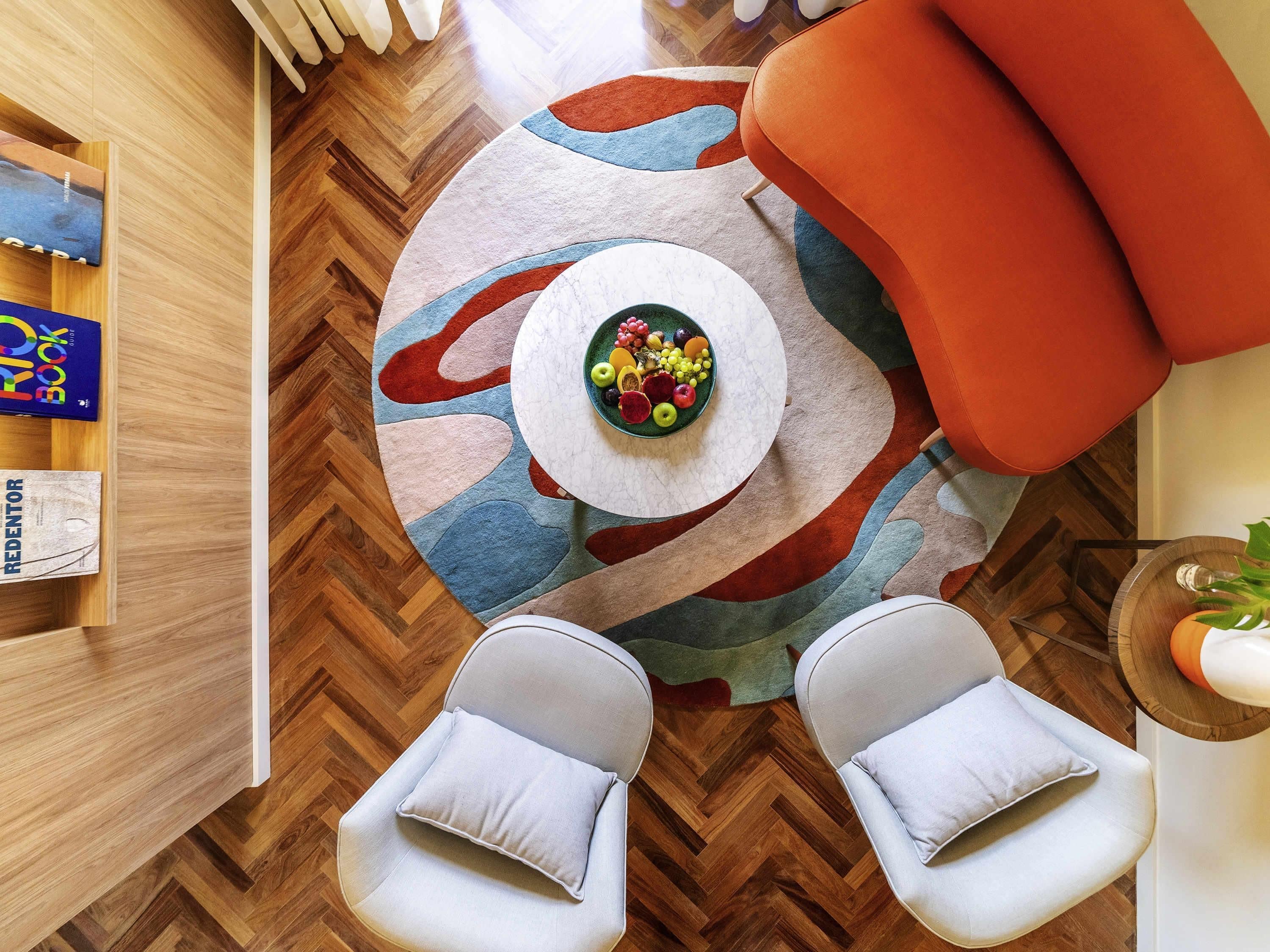 A modern living room with a round coffee table, two white armchairs, a colorful rug, and a wooden floor.