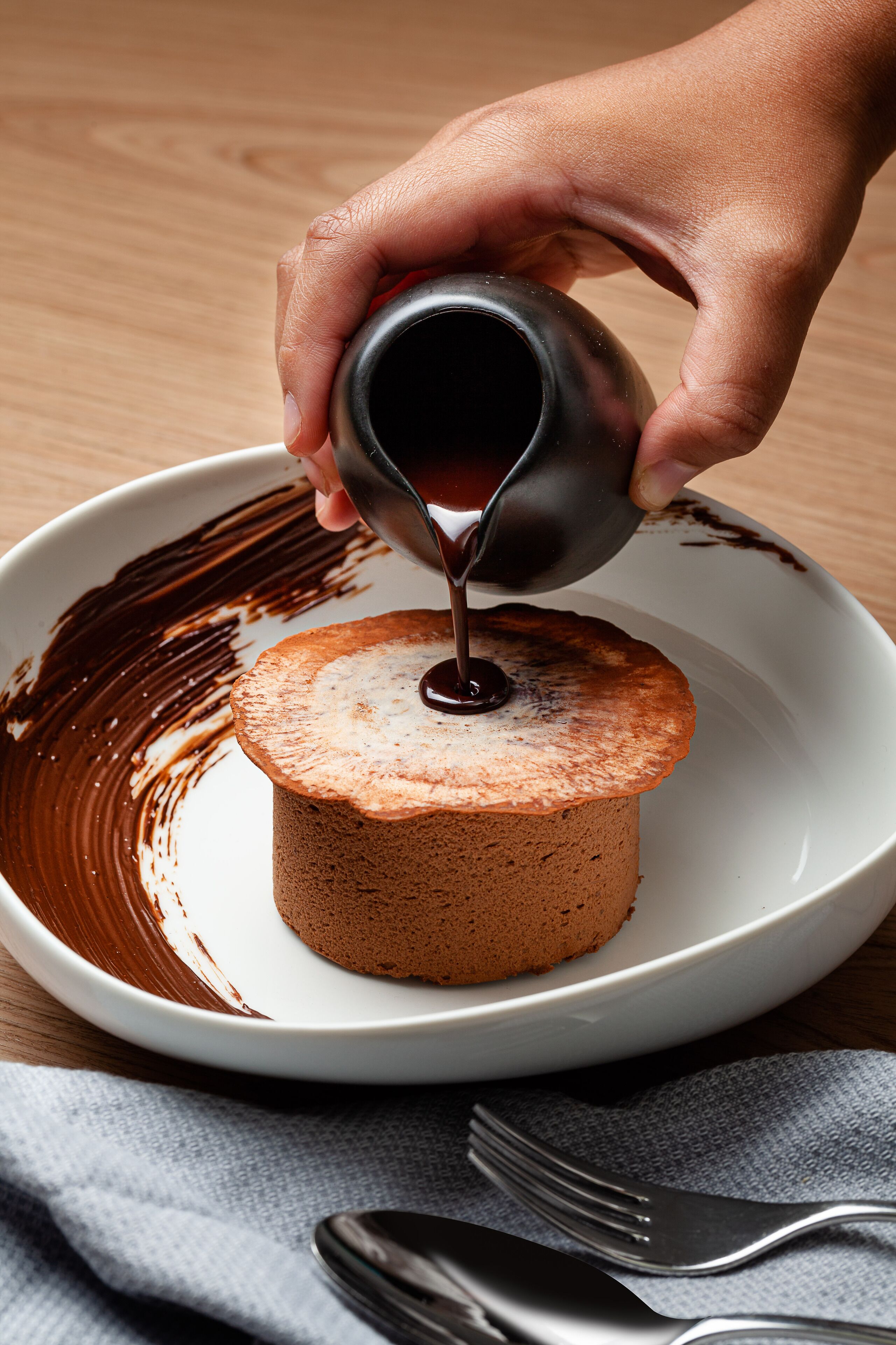 Una mano vertiendo salsa de chocolate sobre un pastel en un plato blanco.