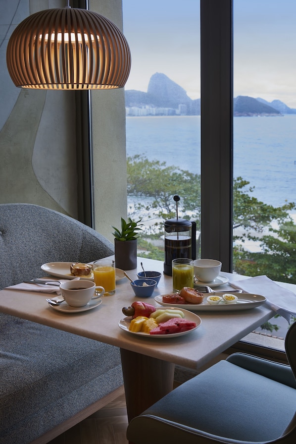 A breakfast table with a view of the sea, a hanging light fixture, and a potted plant.