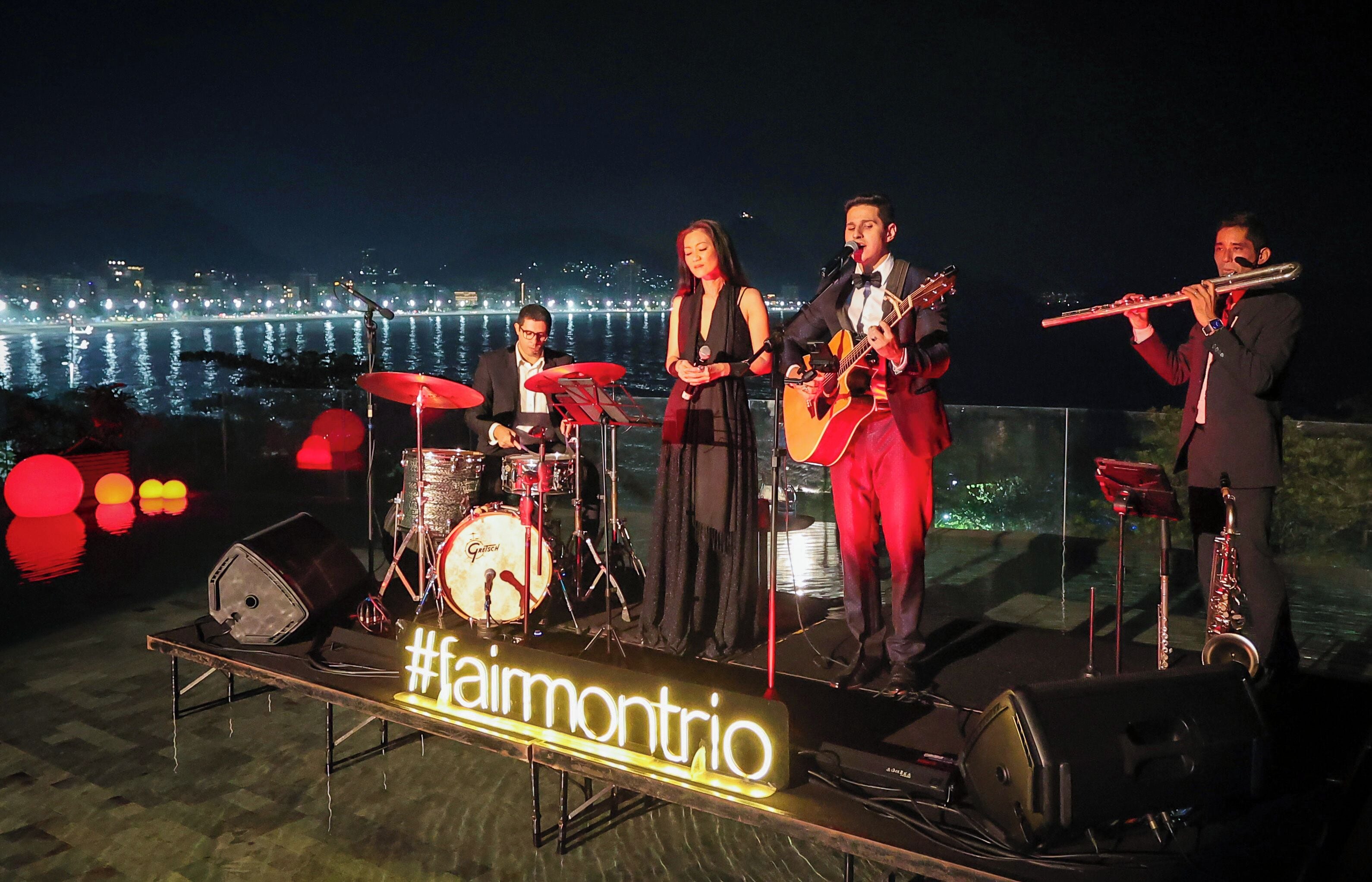 A band performing on an outdoor stage with a city skyline in the background.