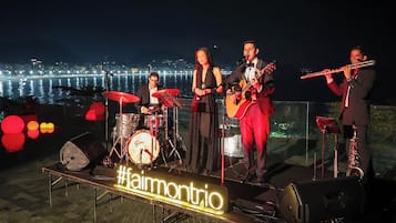 A band performing on an outdoor stage with a city skyline in the background.