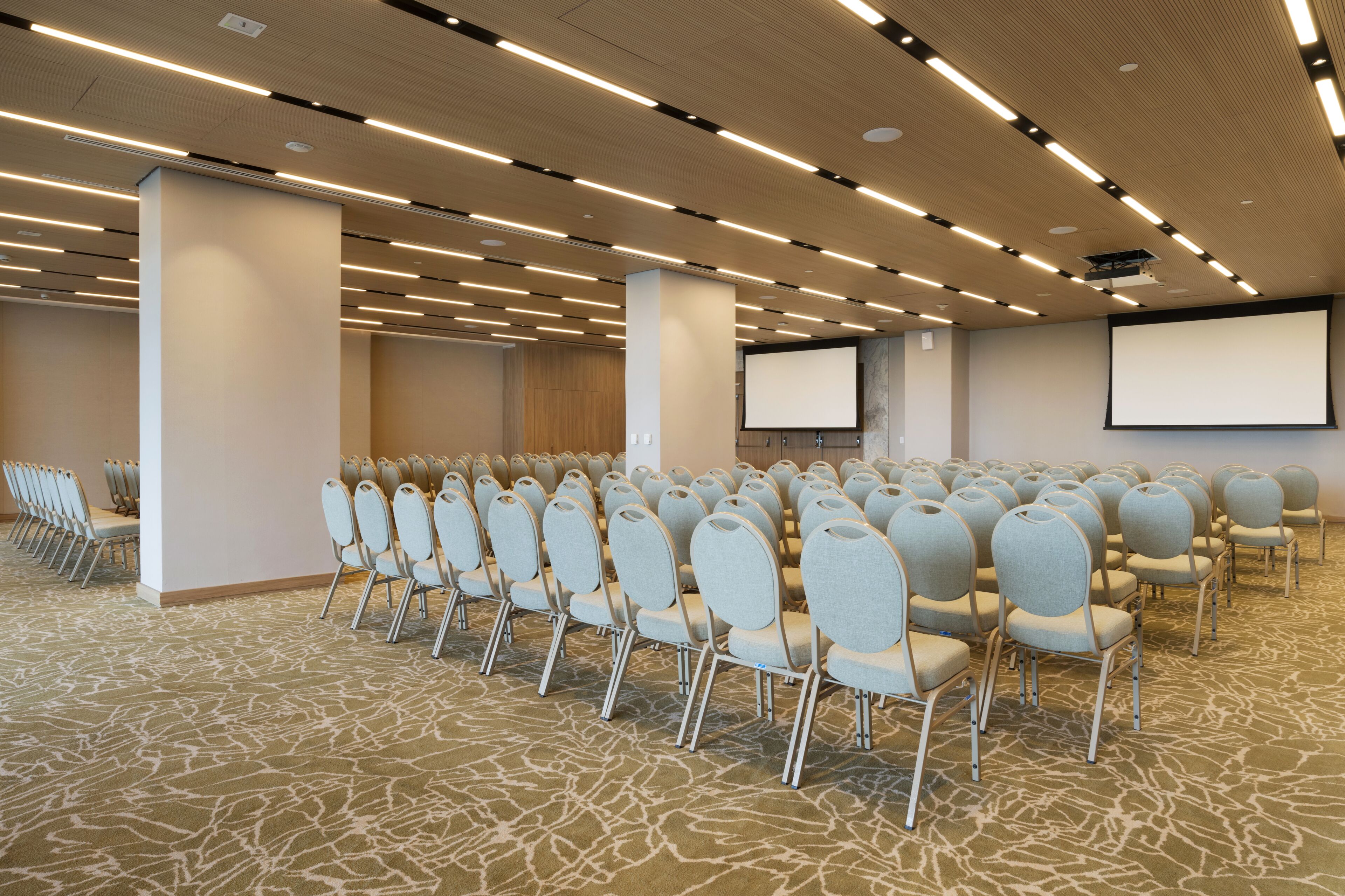 A conference room with rows of chairs, a large screen, and a carpeted floor.