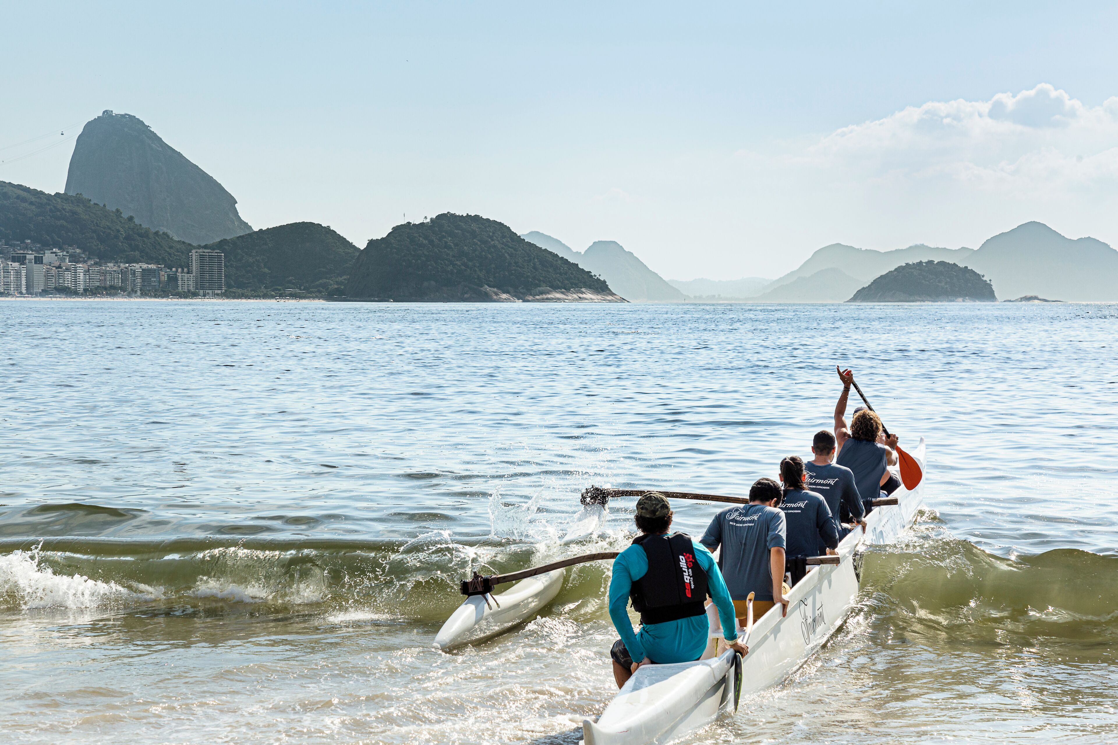 A group of people rowing in a boat on a body of water with mountains in the background.