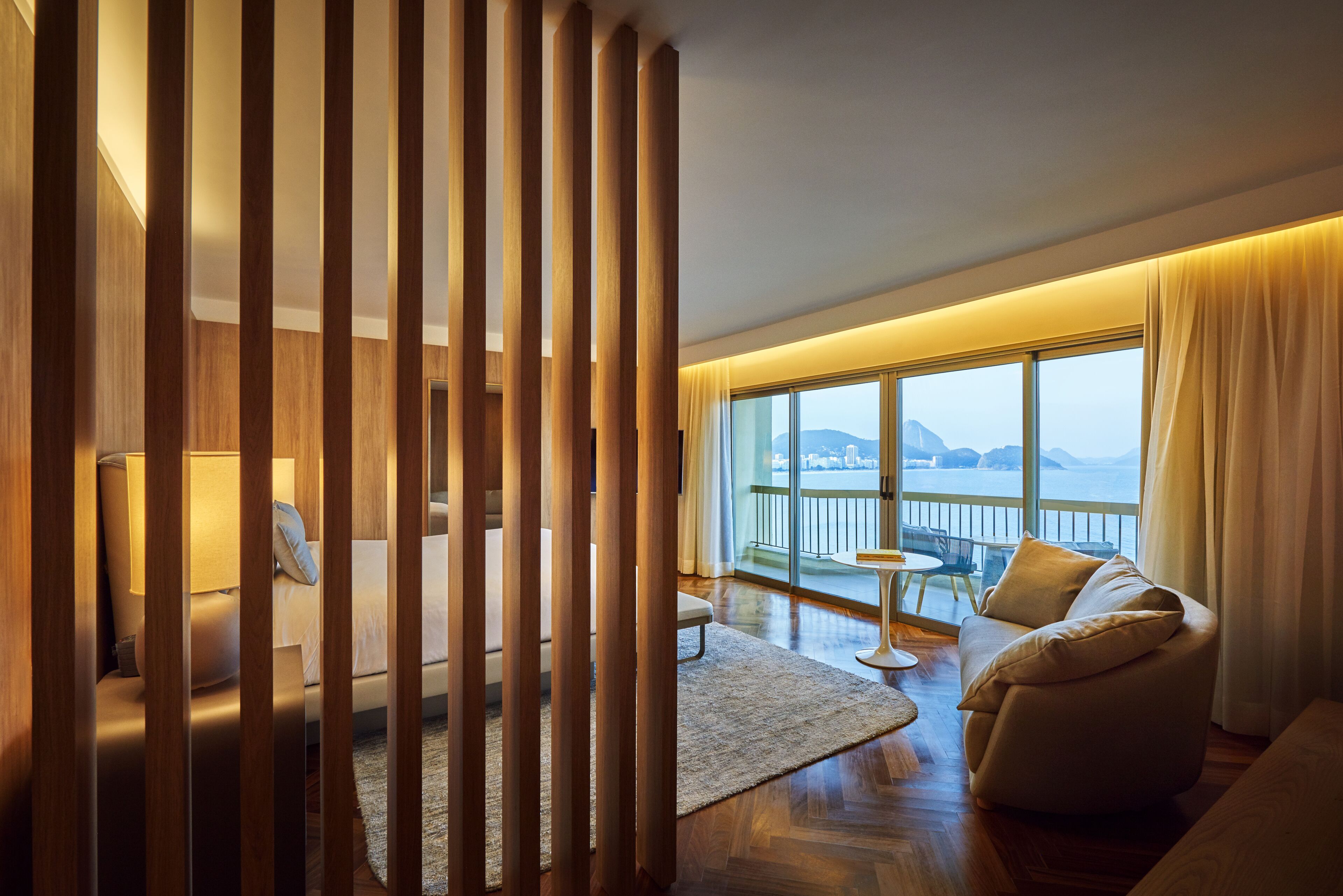 Una habitación de hotel moderna con balcón, listones de madera, un sofá, una mesita y vistas al mar.