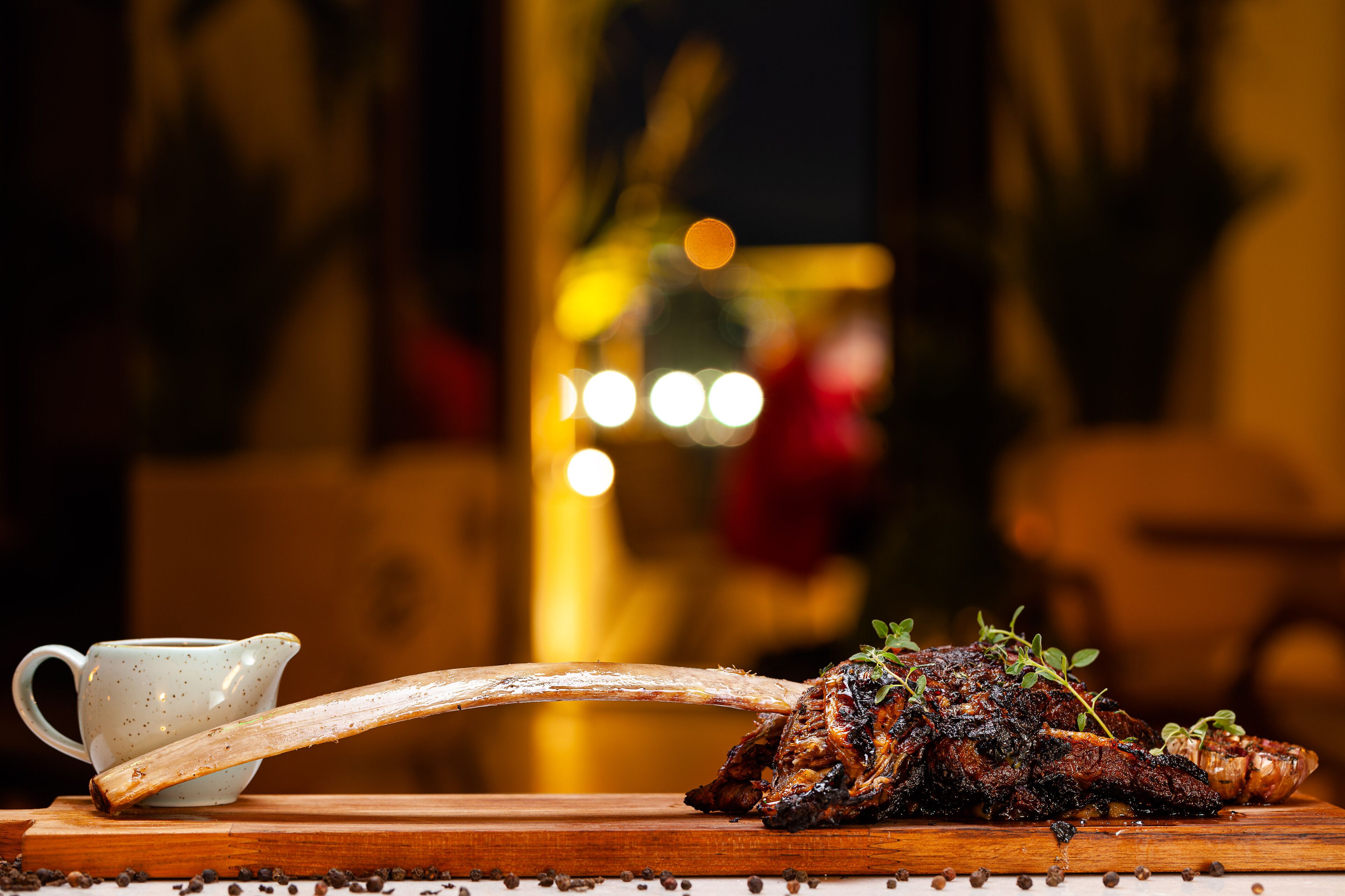 A roasted lamb leg on a wooden board with a white pitcher and a wooden spoon.
