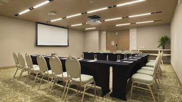 Un salón de conferencias con una larga mesa, sillas, una pantalla de proyector y suelo alfombrado.