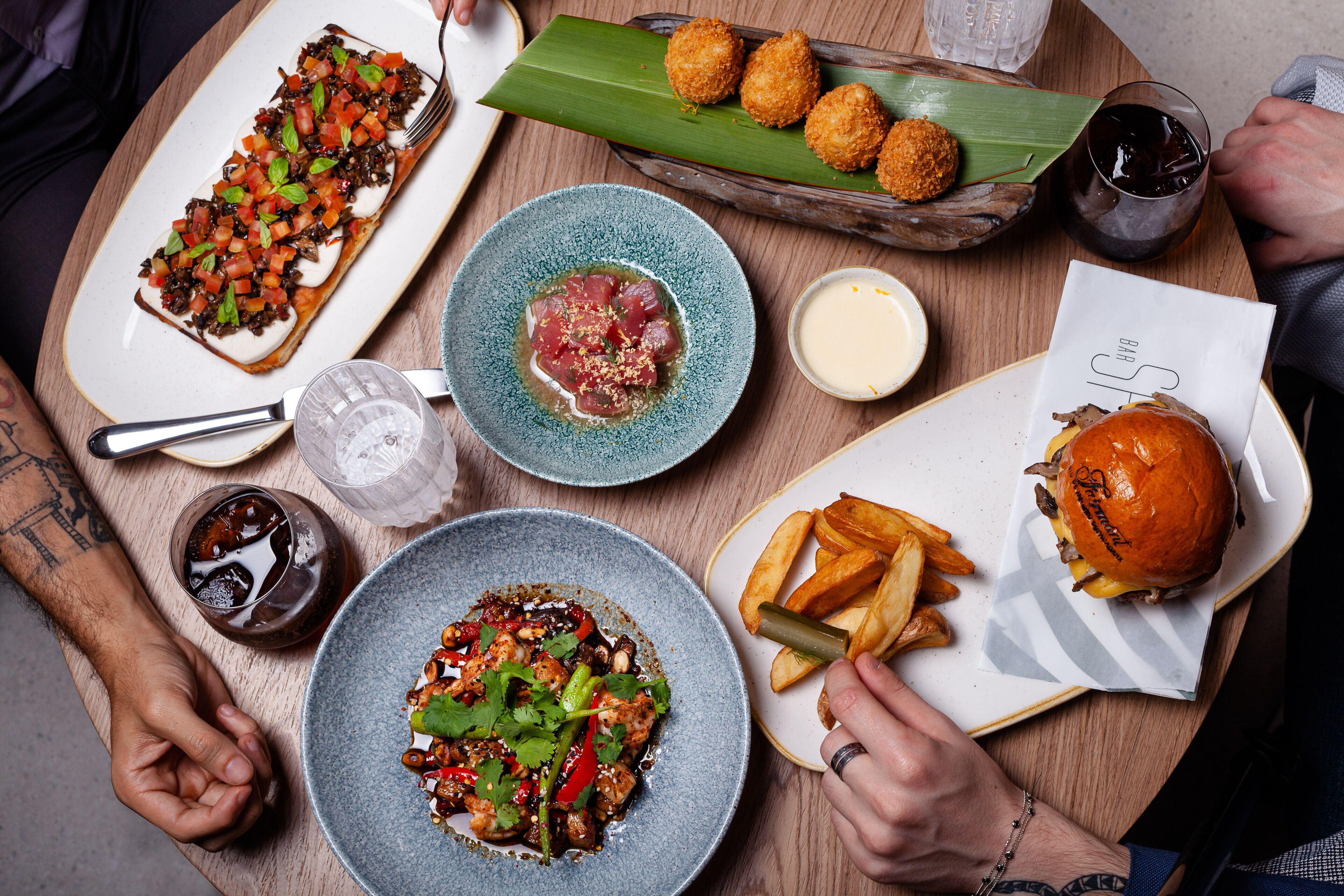 A table with various dishes including a burger, fries, and a plate of ceviche, along with drinks and a menu.