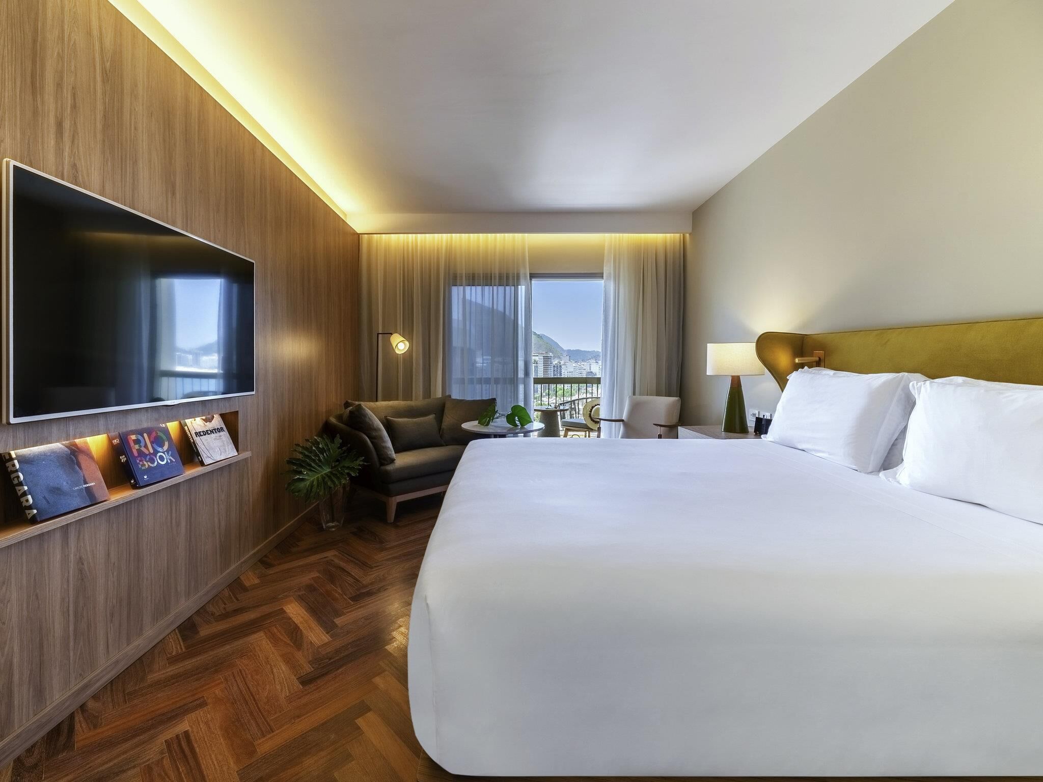 Una camera d'albergo con un letto grande, una televisione a schermo piatto montata a parete, un divano, un tavolino e vista sulla città.