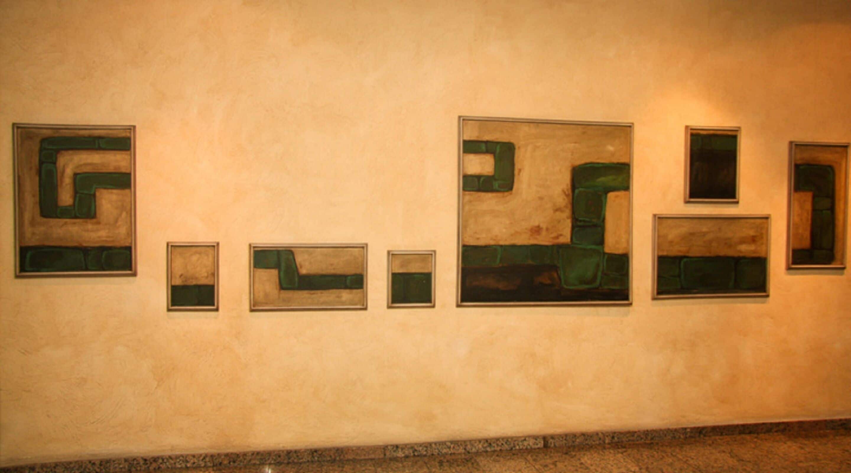A series of framed abstract artworks on a plain wall.