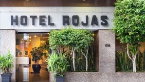 Exterior del Hotel Rojas, con entrada despejada, plantas en macetas y fachada de piedra.