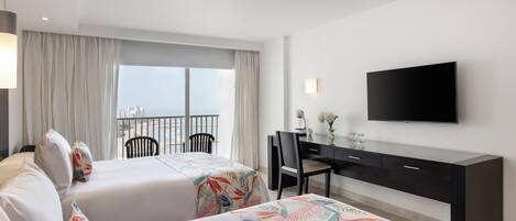 Habitación de hotel con dos camas, un escritorio, una silla, un televisor y un balcón con vistas.