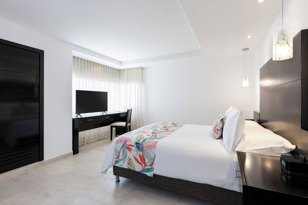 A modern hotel room with a large bed, a desk, and a flat-screen TV.