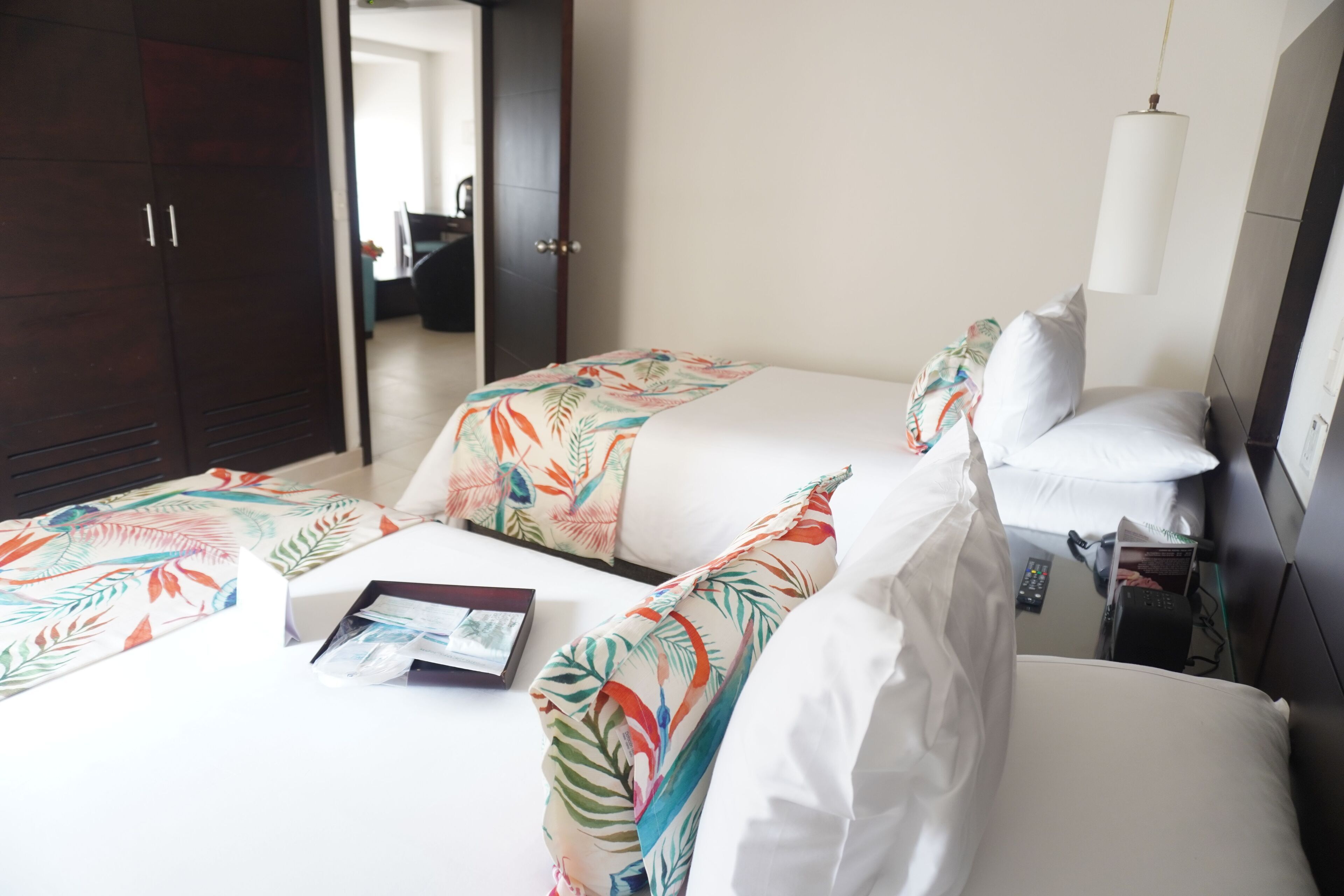 Een hotelkamer met twee bedden, elk voorzien van een bloemenprint beddeken, een nachtkastje met een lamp en een kledingkast.