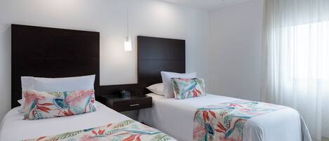 A hotel room with two beds, each with a floral bedspread, a dark headboard, a bedside table, and a nightstand.