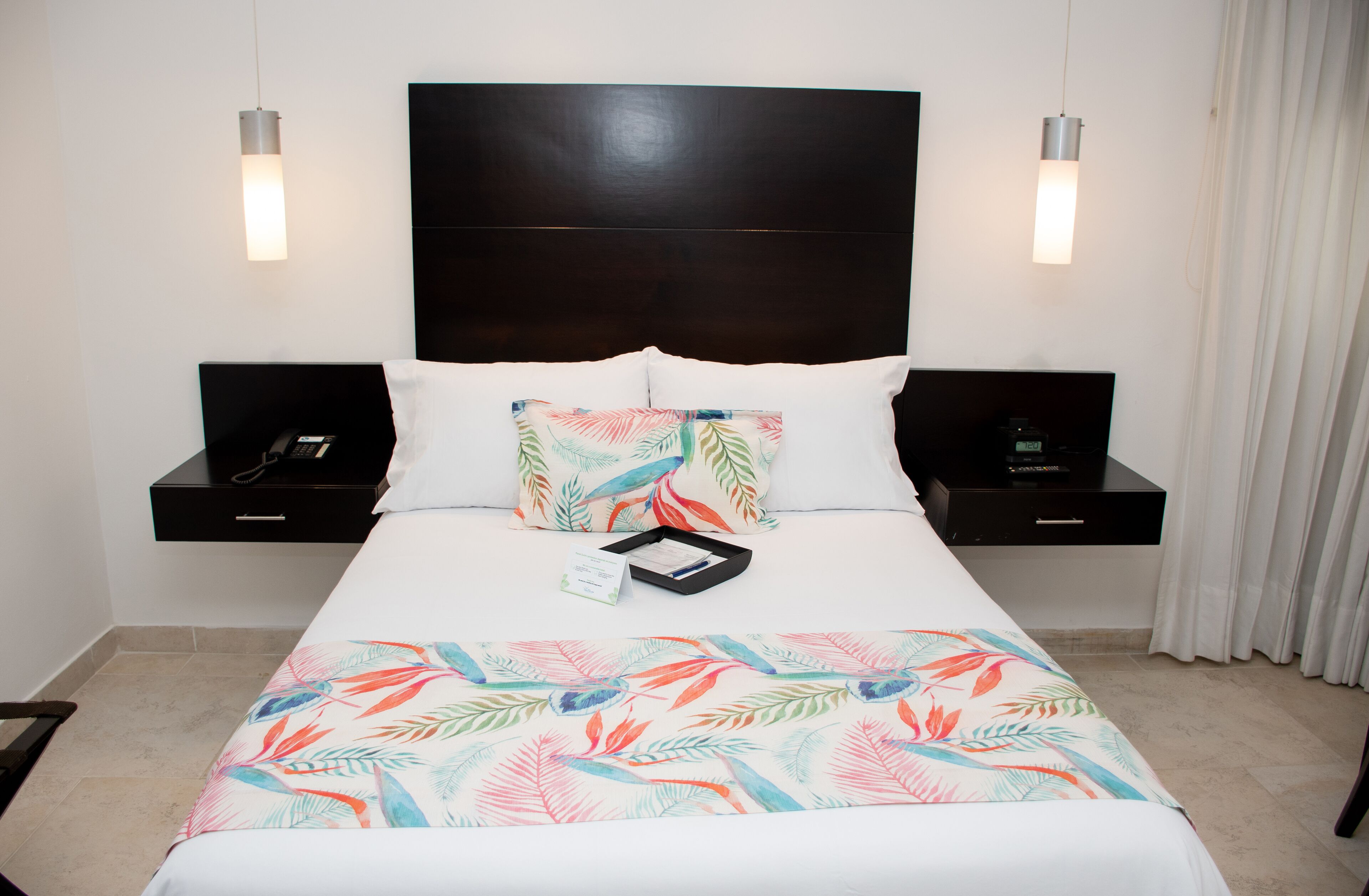 A hotel room with a large bed, two bedside tables, a headboard, and a nightstand with a phone and a lamp.