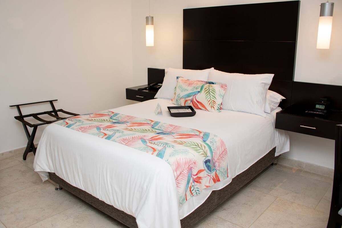 A neatly made bed with a floral bedspread, a bedside table with a lamp, and a nightstand with a phone and alarm clock.