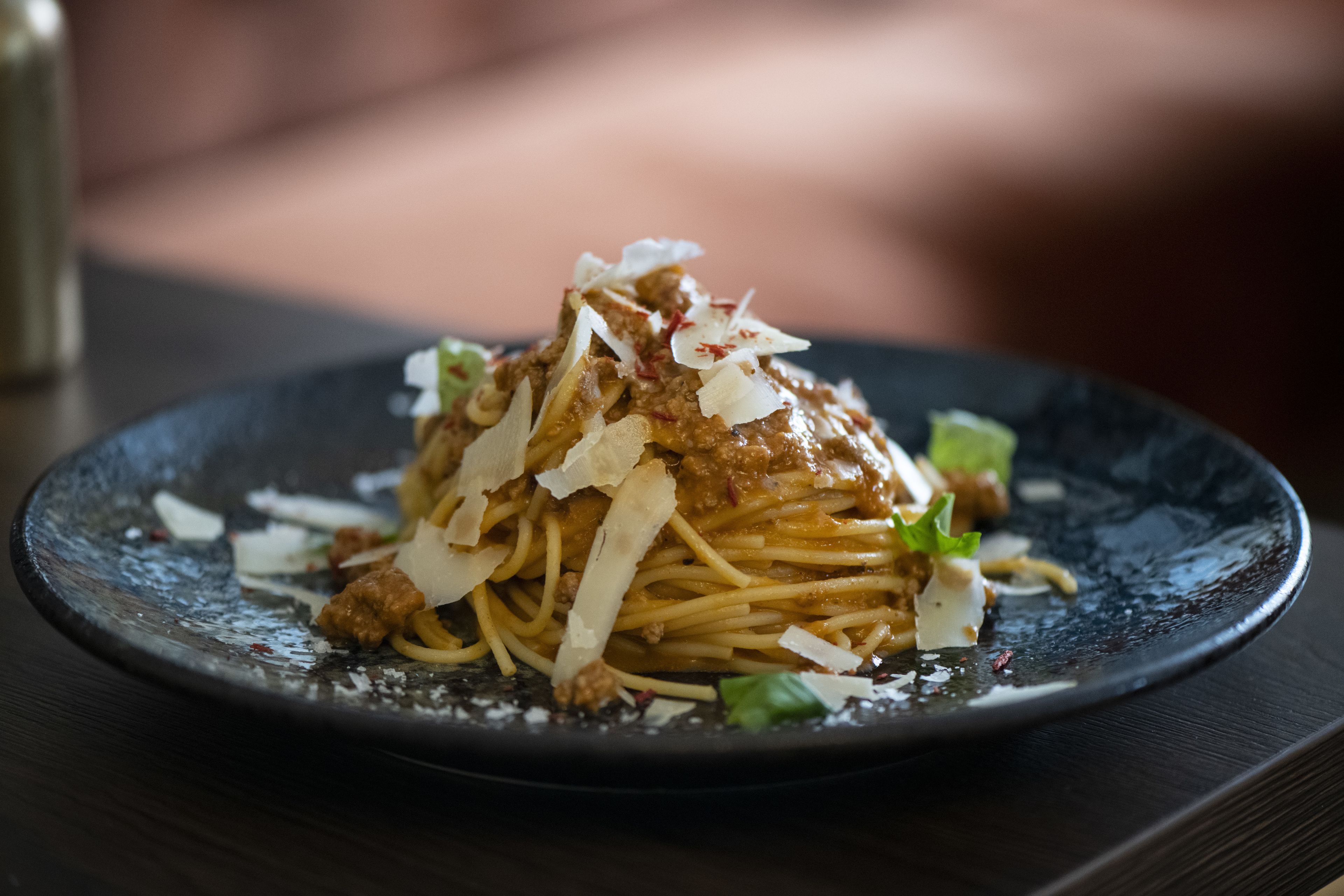 A plate of spaghetti with meat sauce and grated cheese on a dark plate.