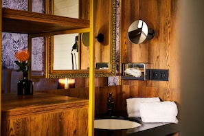 A bathroom with wooden paneling, a wooden vanity with a mirror, a sink, and a towel rack. - Hotel Palais26 (Villach)