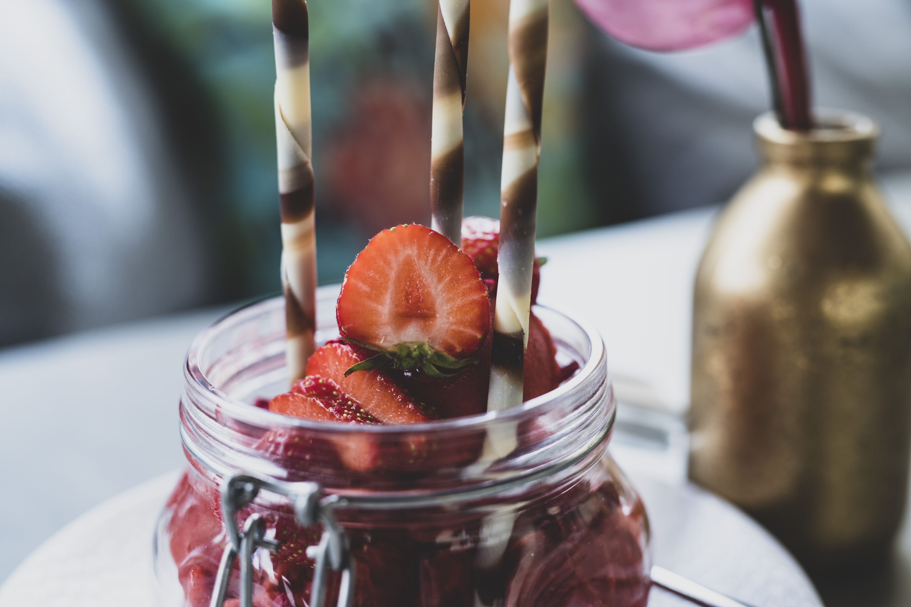 Un frasco de vidrio lleno de fresas y una cuchara de metal.
