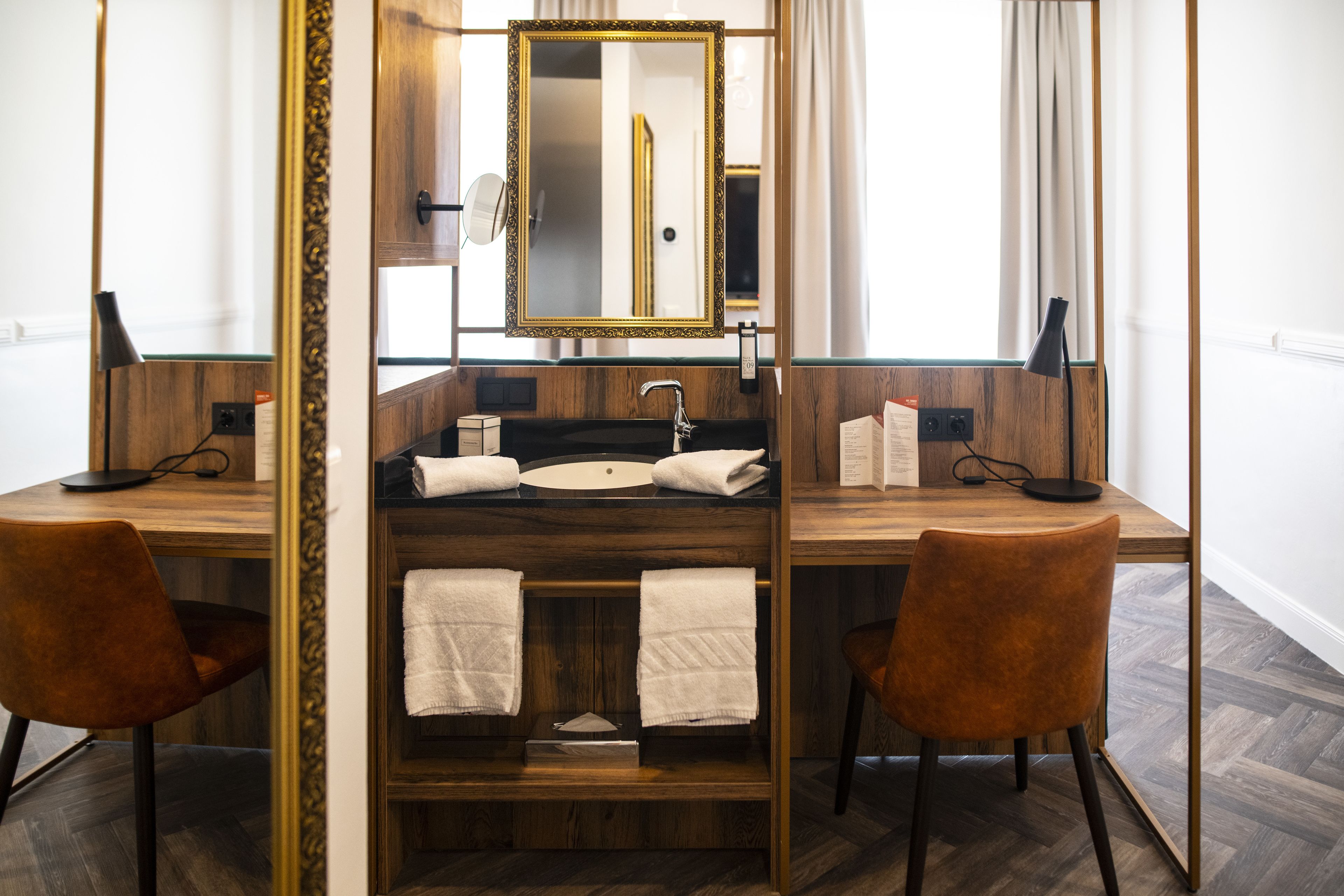 A modern bathroom with a wooden vanity, a large mirror, and two chairs.