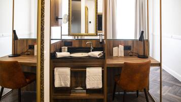 A modern bathroom with a wooden vanity, a large mirror, and two chairs.
