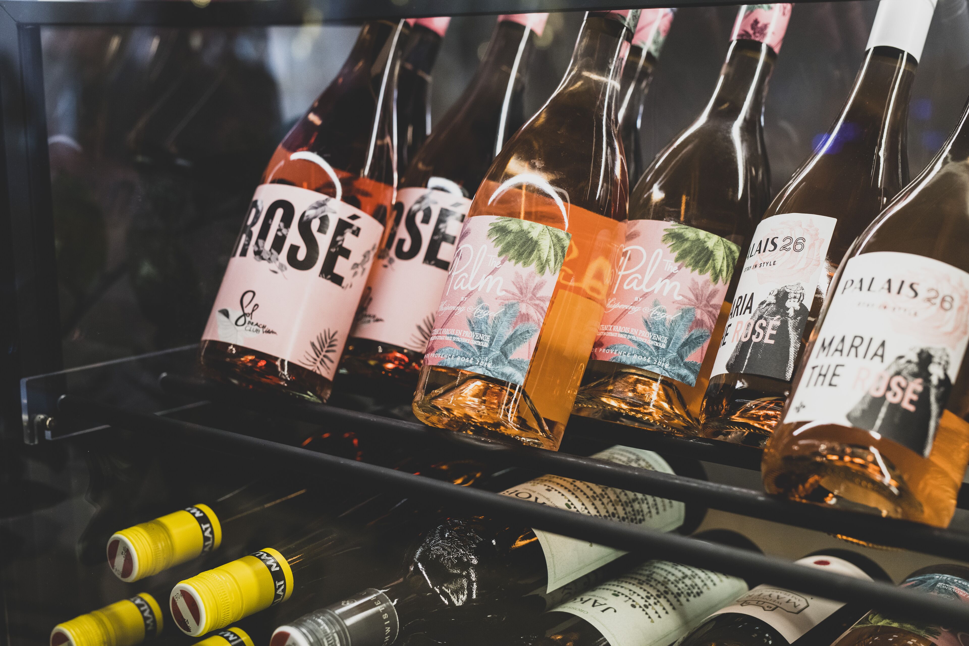 A display of wine bottles with labels, some with text and others with images, arranged on a shelf.