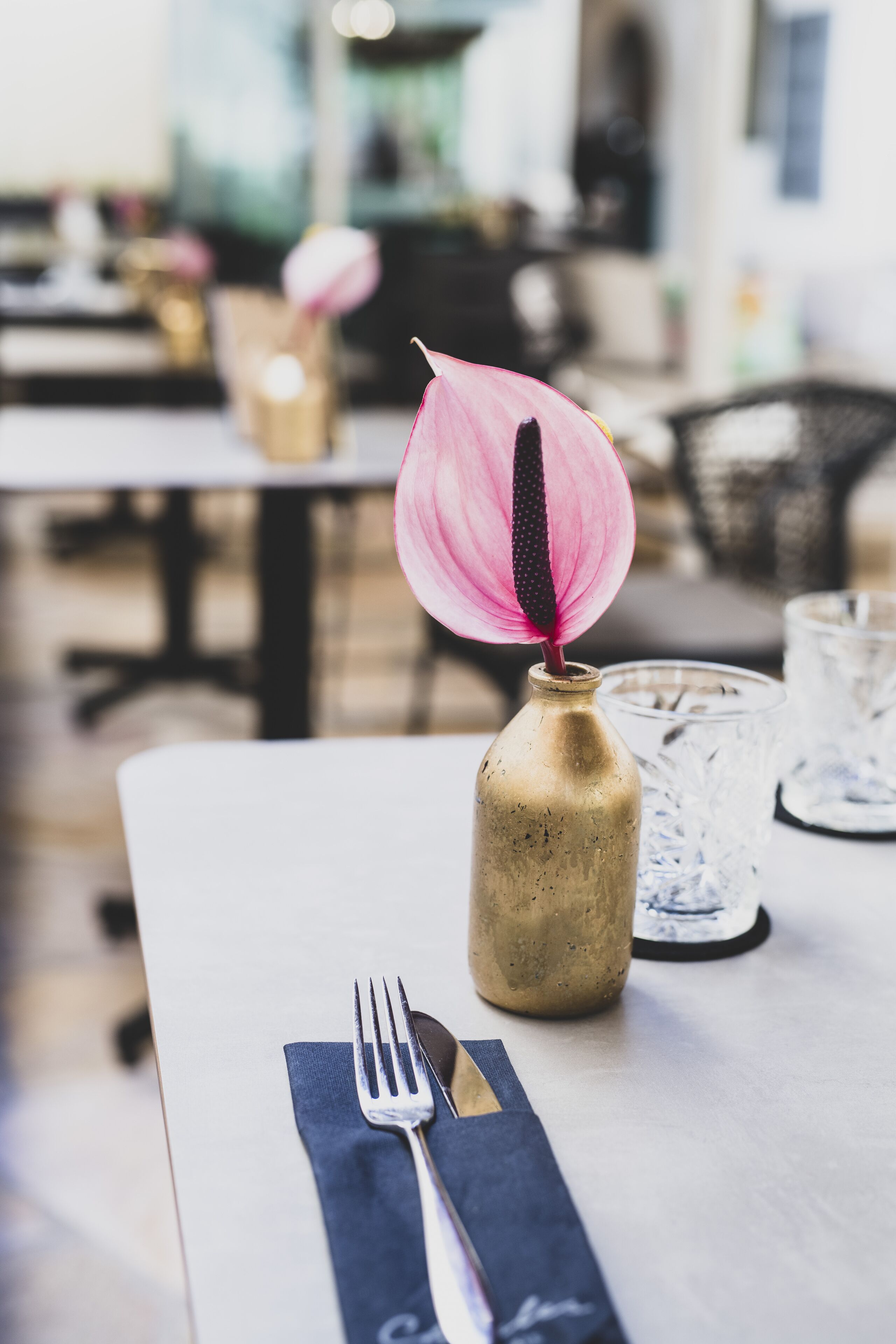 Ein Esstisch mit einer Vase, die eine rosa Blume, eine Gabel und ein Servietttuch enthält.