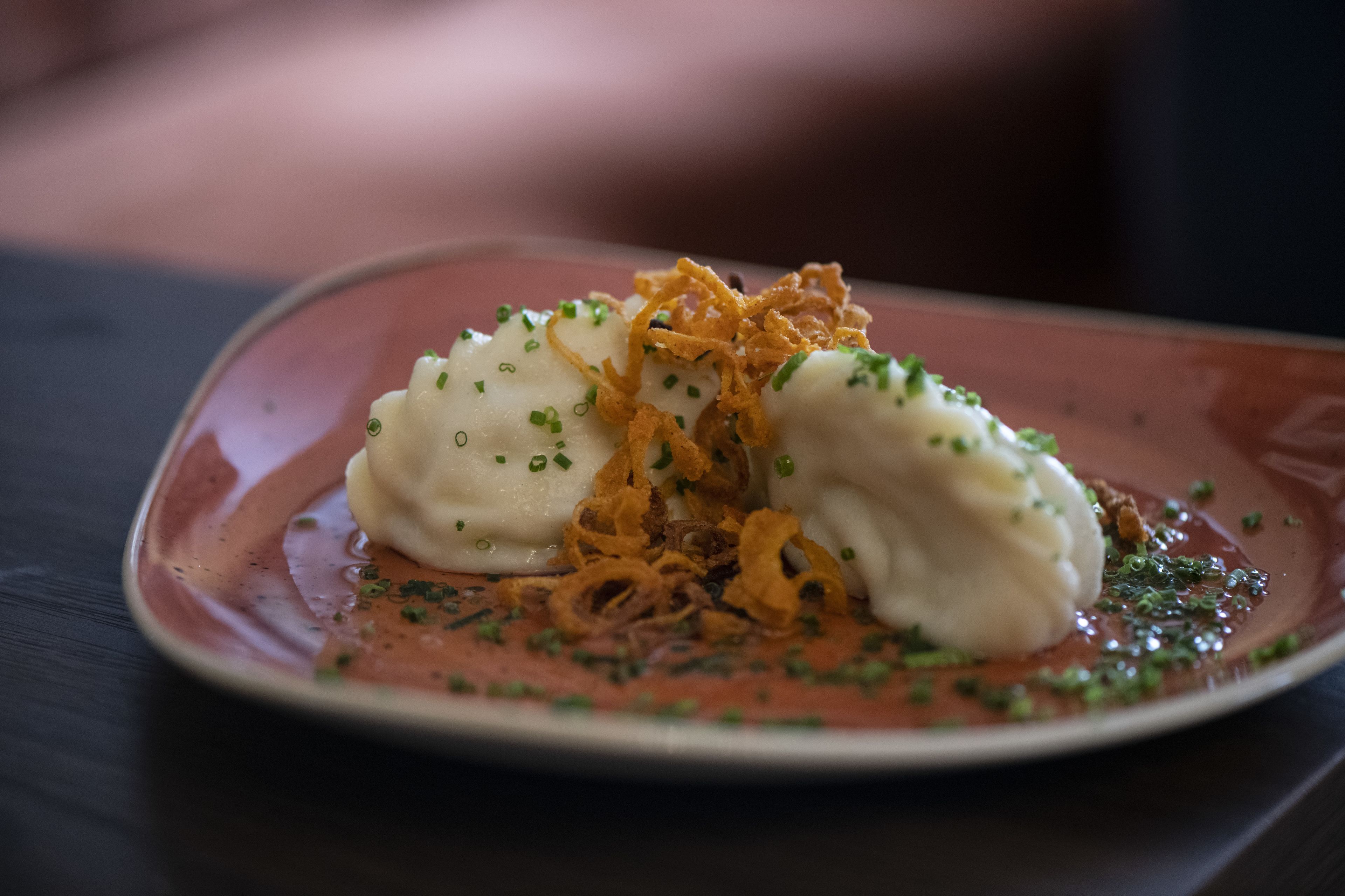 Een bord met dumplings, gebakken uien en groene garnering.