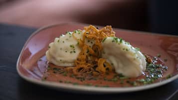 Een bord met dumplings, gebakken uien en groene garnering.
