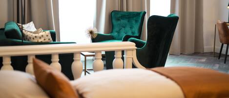 A bedroom with a green armchair, a white bed with brown pillows, and a small table with a decorative item.