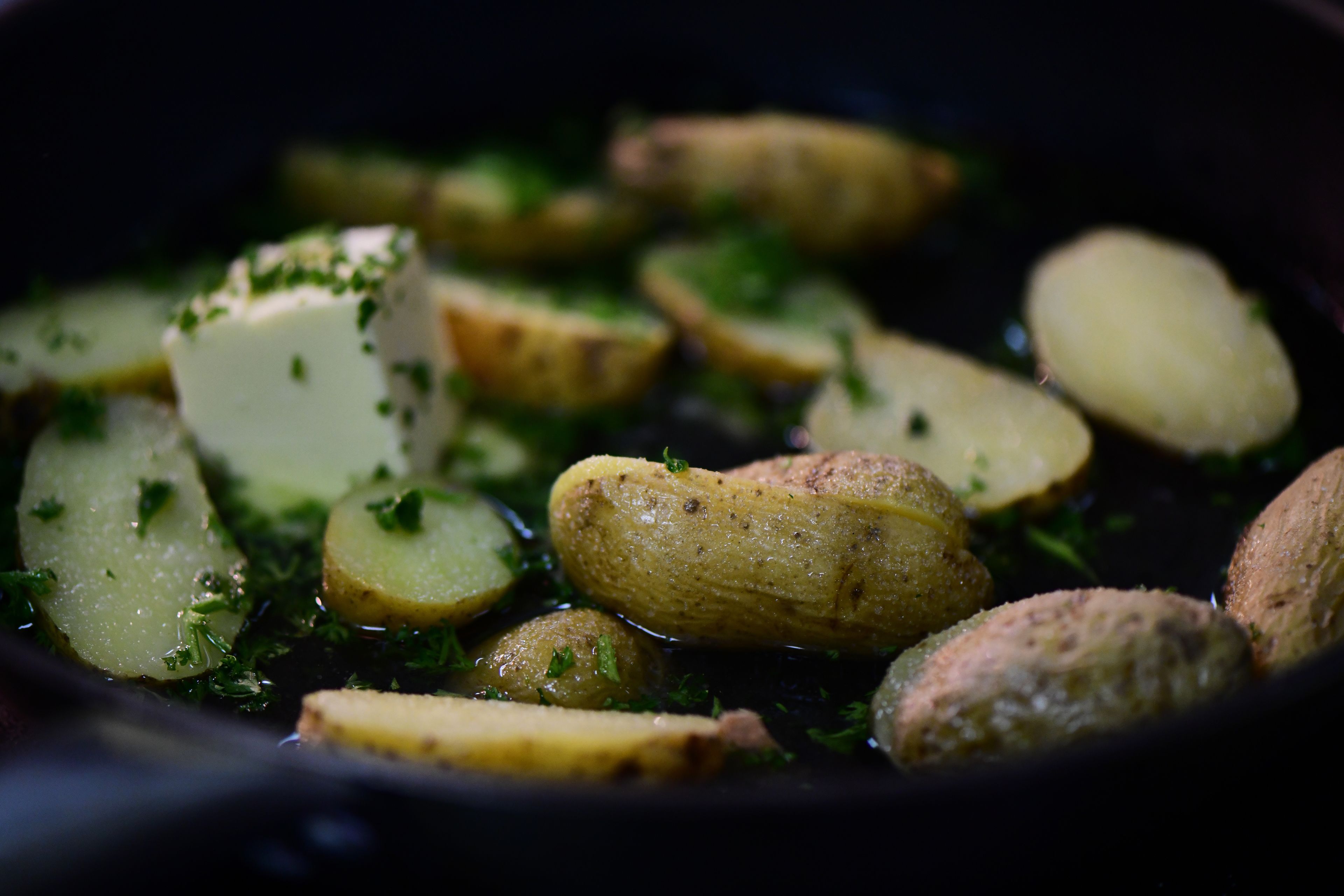 A close-up of sliced potatoes in a pan with herbs.