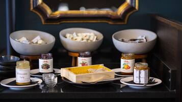 A breakfast setup with three bowls of food, two jars of jam, a honey dish, and a small jar of butter on a table.